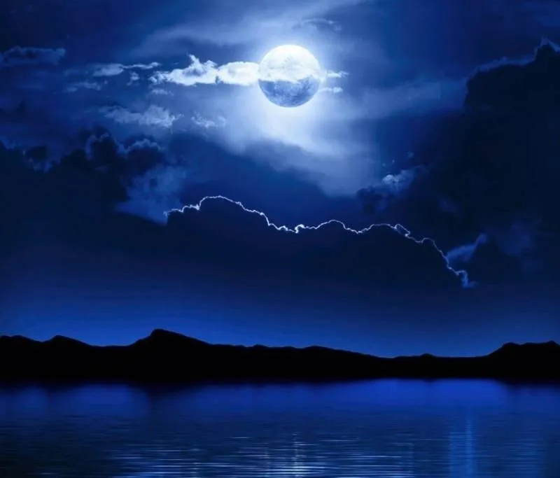 Full Moon Glowing Behind Clouds Over Dark Mountain Lake