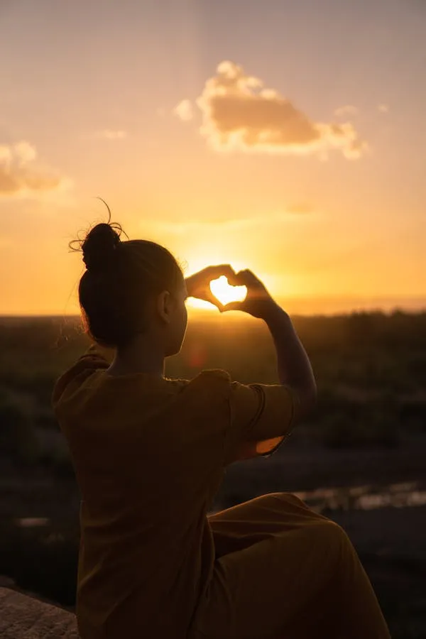 Girl Forming Heart Shape with Hands During Sunset Image