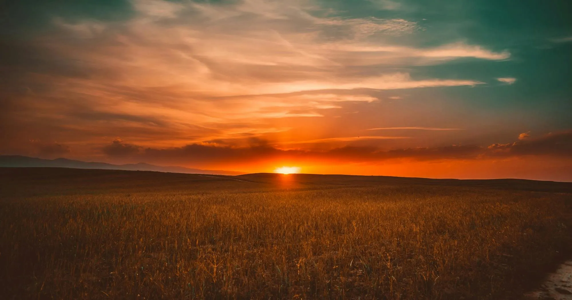 Glowing Sunset Clouds Over Open Field and Distant Hills