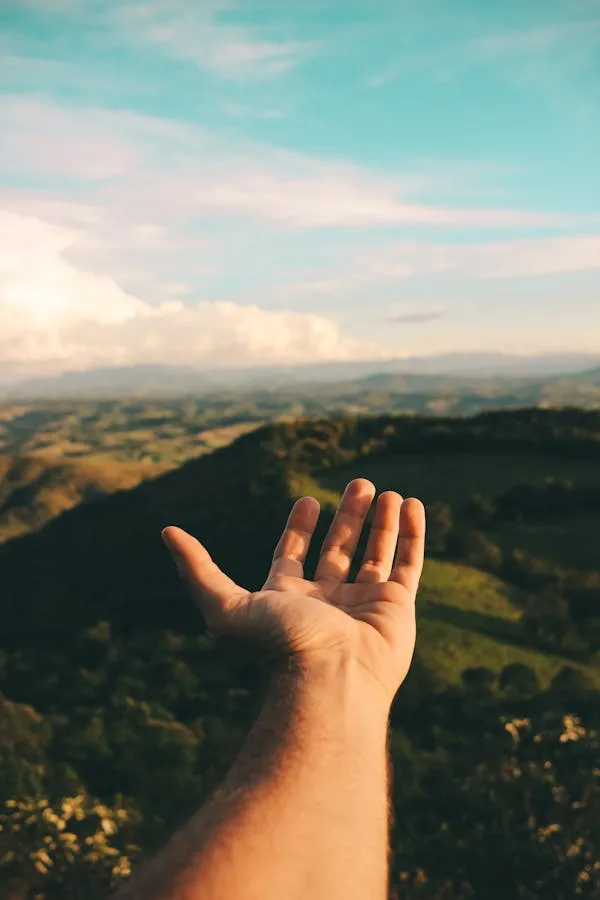 Hand Reaching Out Towards a Scenic Green Hill Landscape