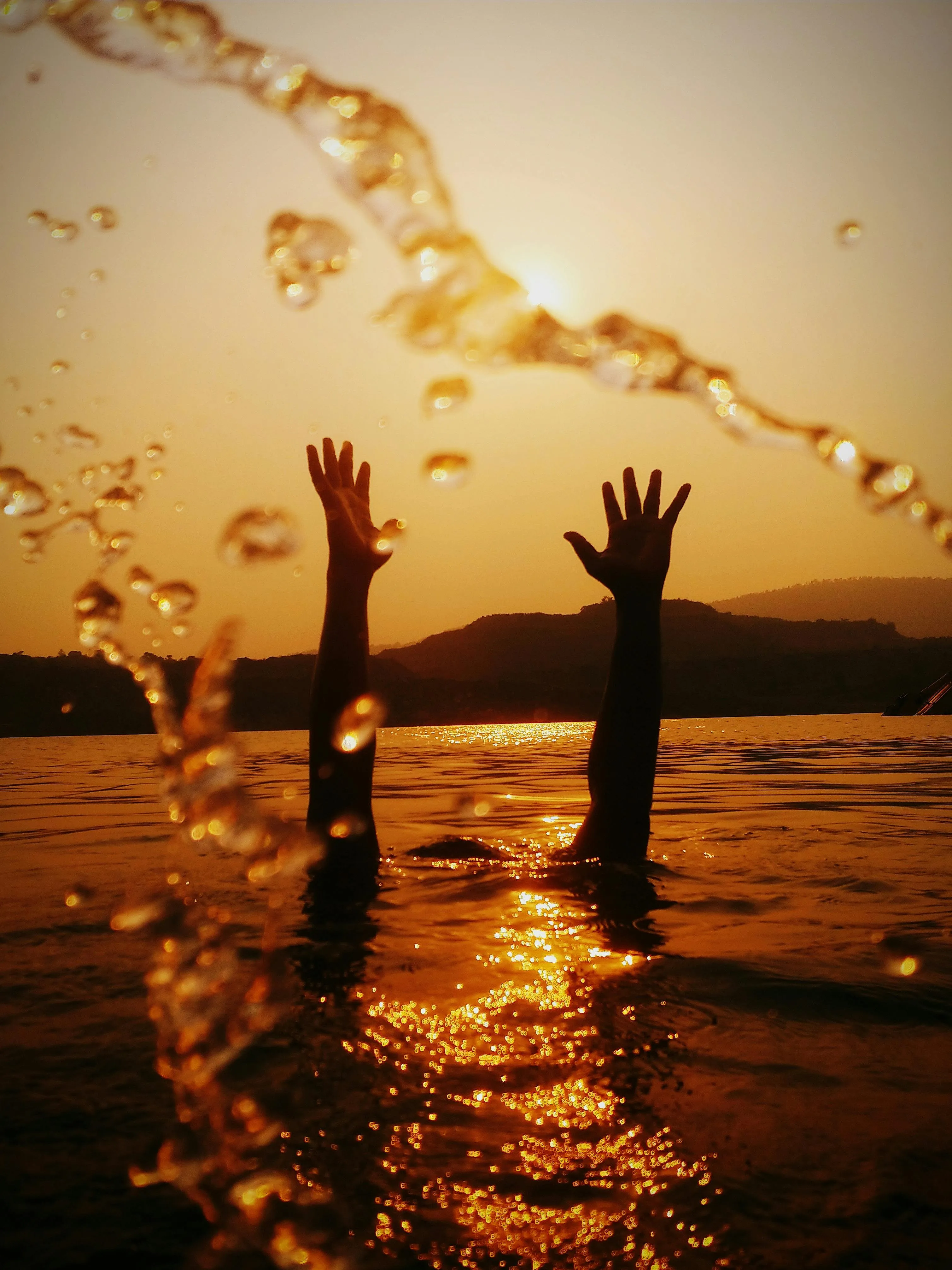 Hands Raised in Water As the Sun Sets on the Horizon
