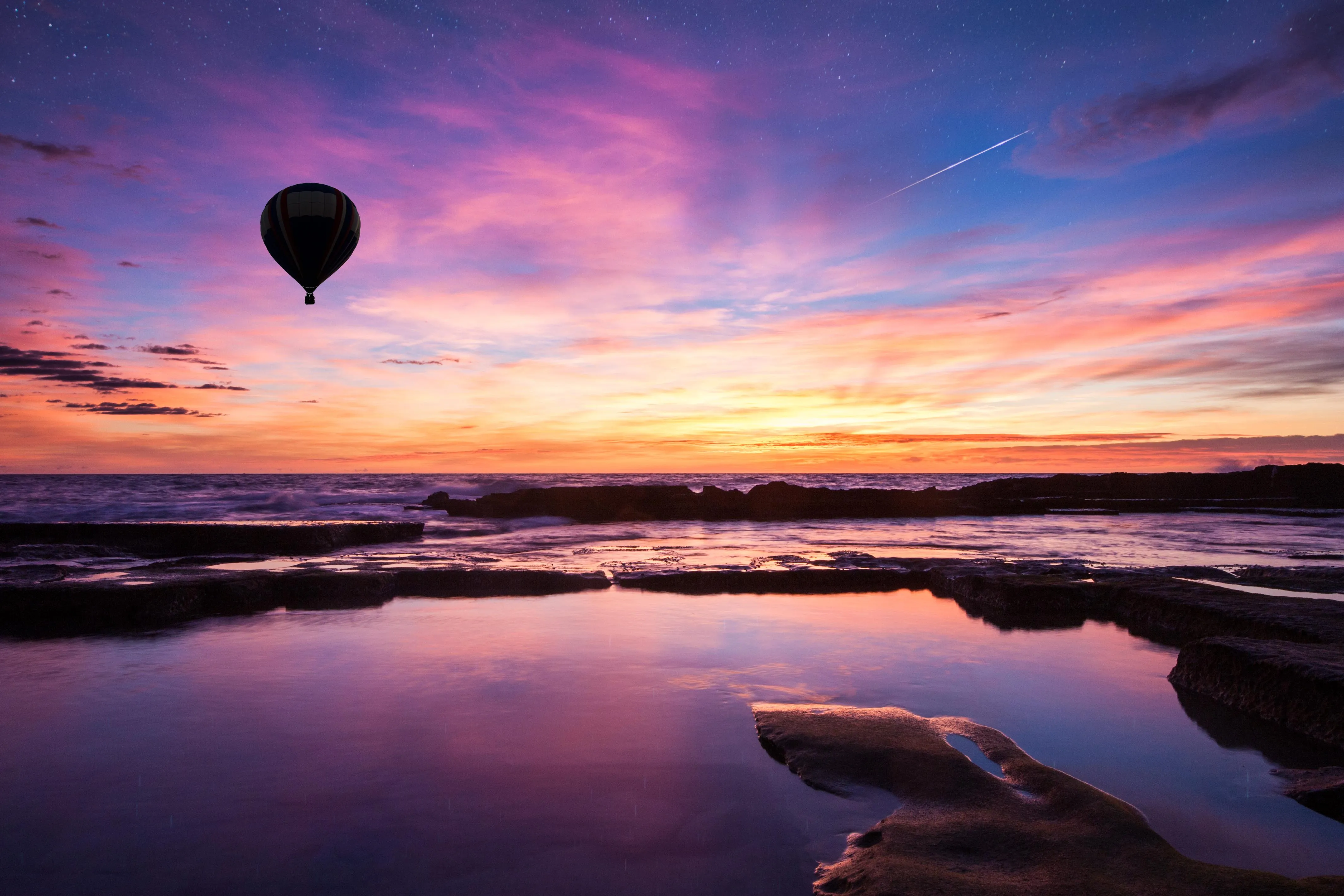 Hot air balloon flying over calm lake during sunset