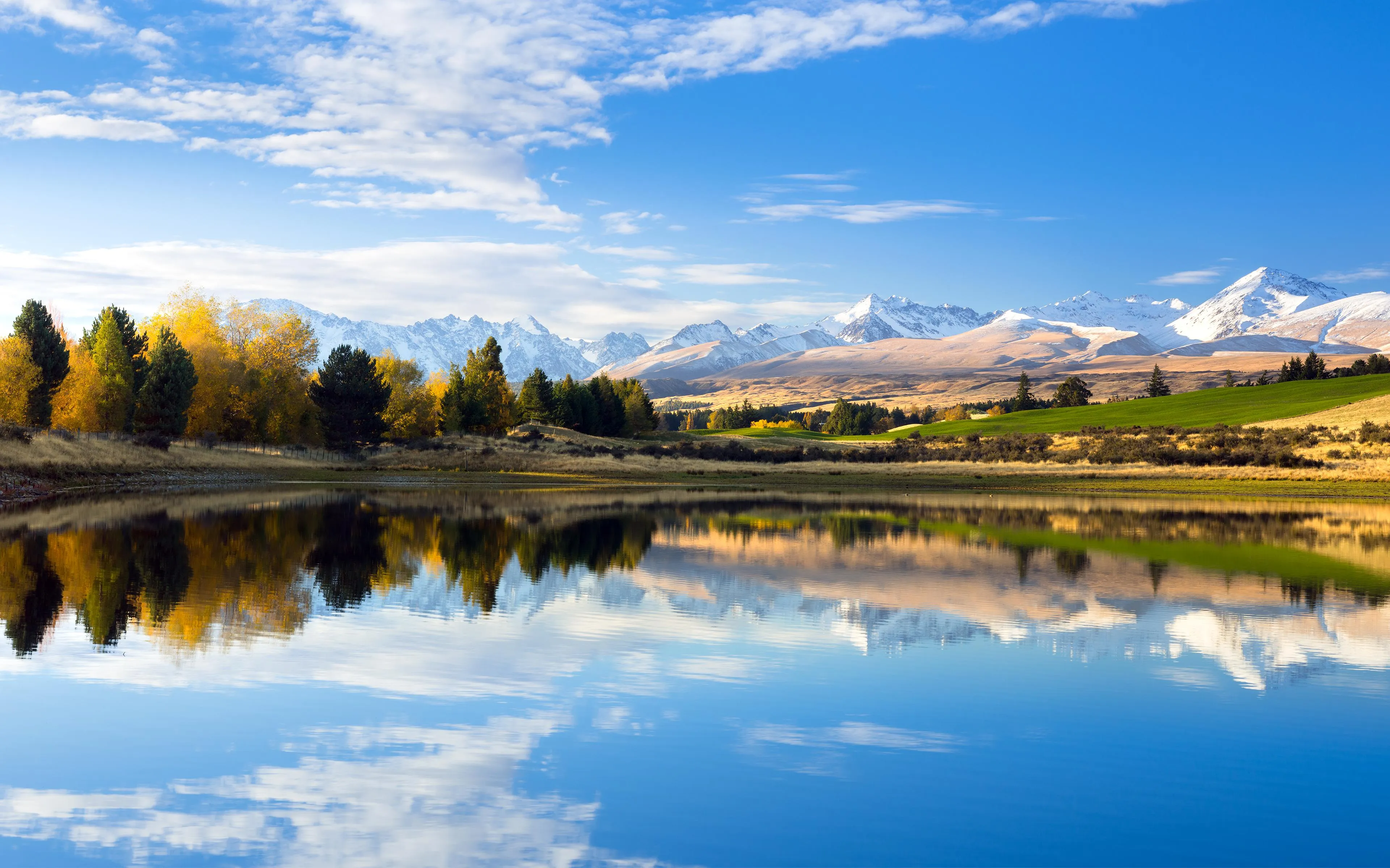 Lake reflecting blue sky with trees and clear clouds