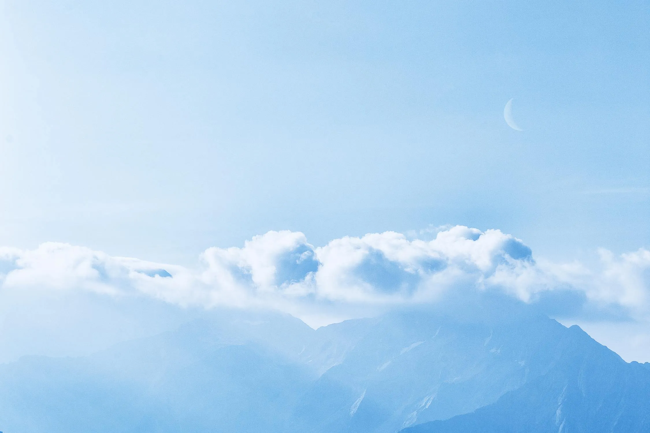 Light Clouds Floating Above Blue Mountains on Clear Day Image