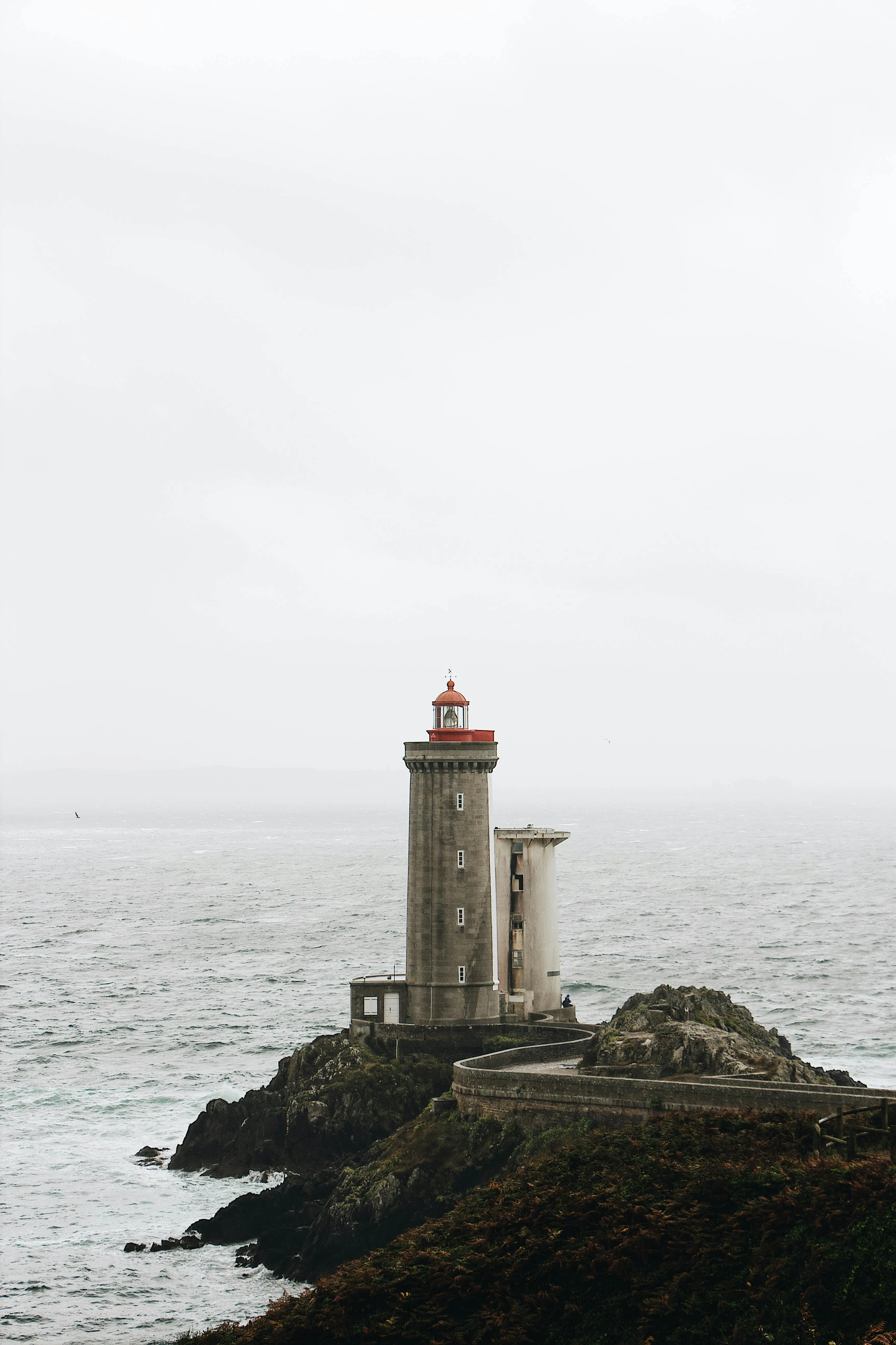 Lighthouse Standing on Rocky Coast Beneath Gray Sky