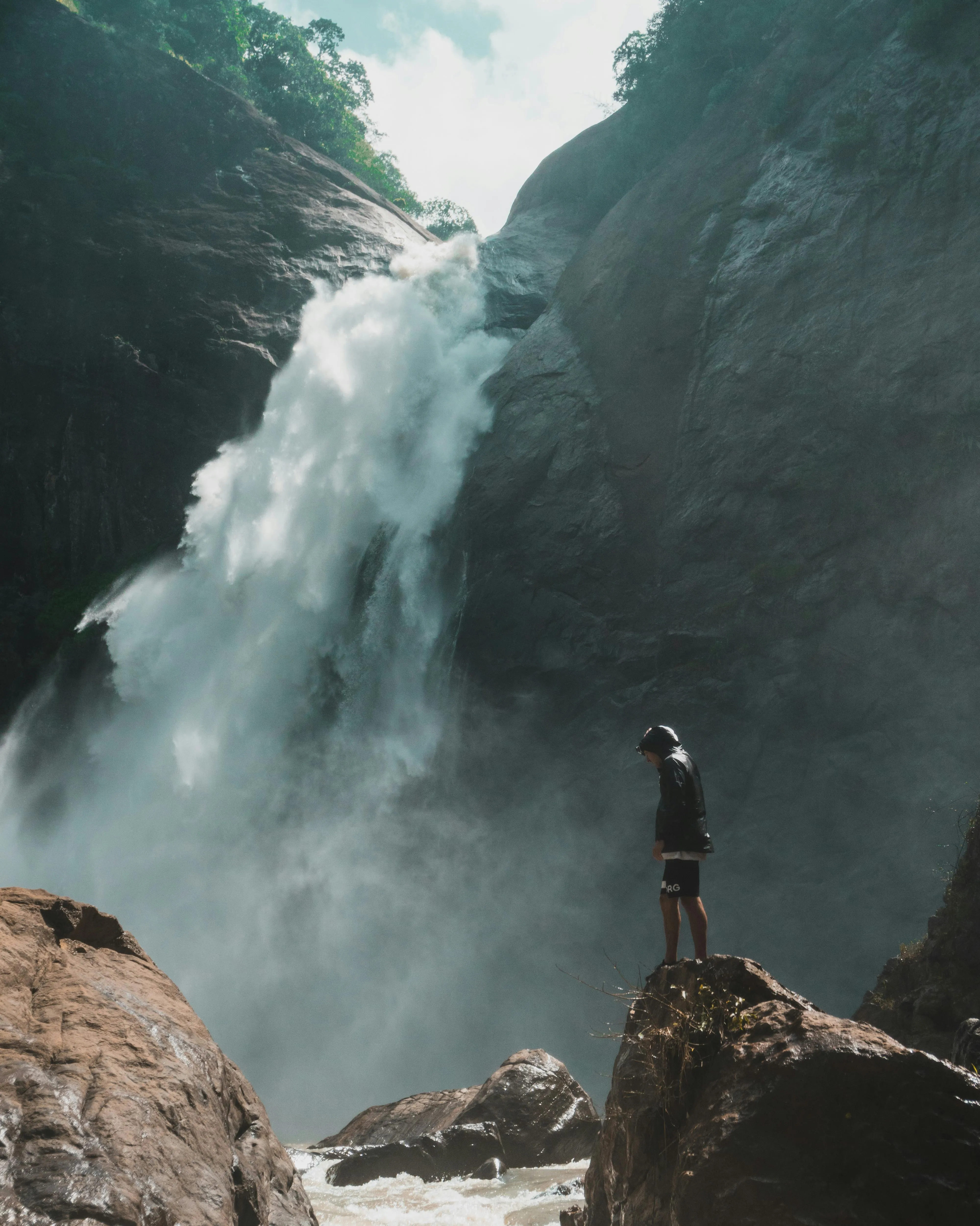 Lone Hiker Standing Near a Powerful Forest Waterfall