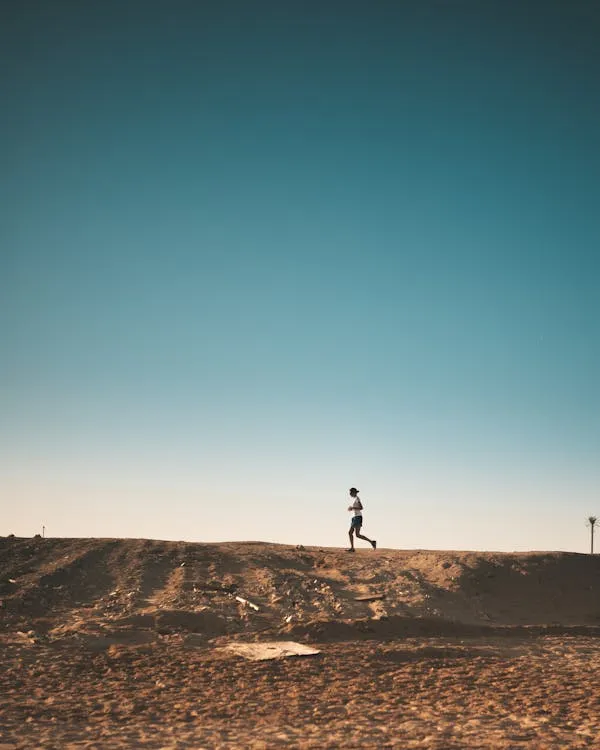 Lone Person Walking on Sand Dunes Under Clear Blue Sky