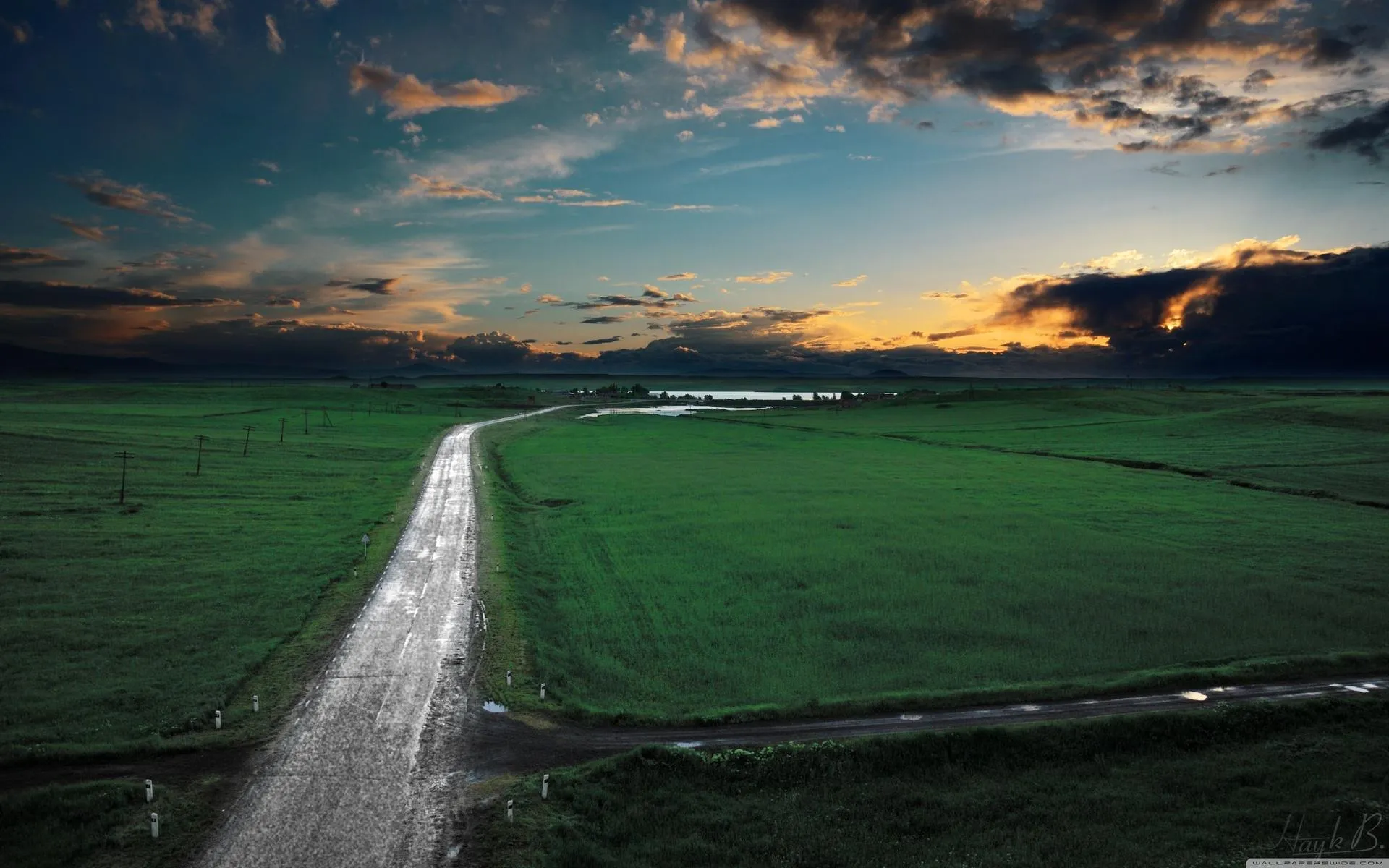 Long road through lush green fields under cloudy sky