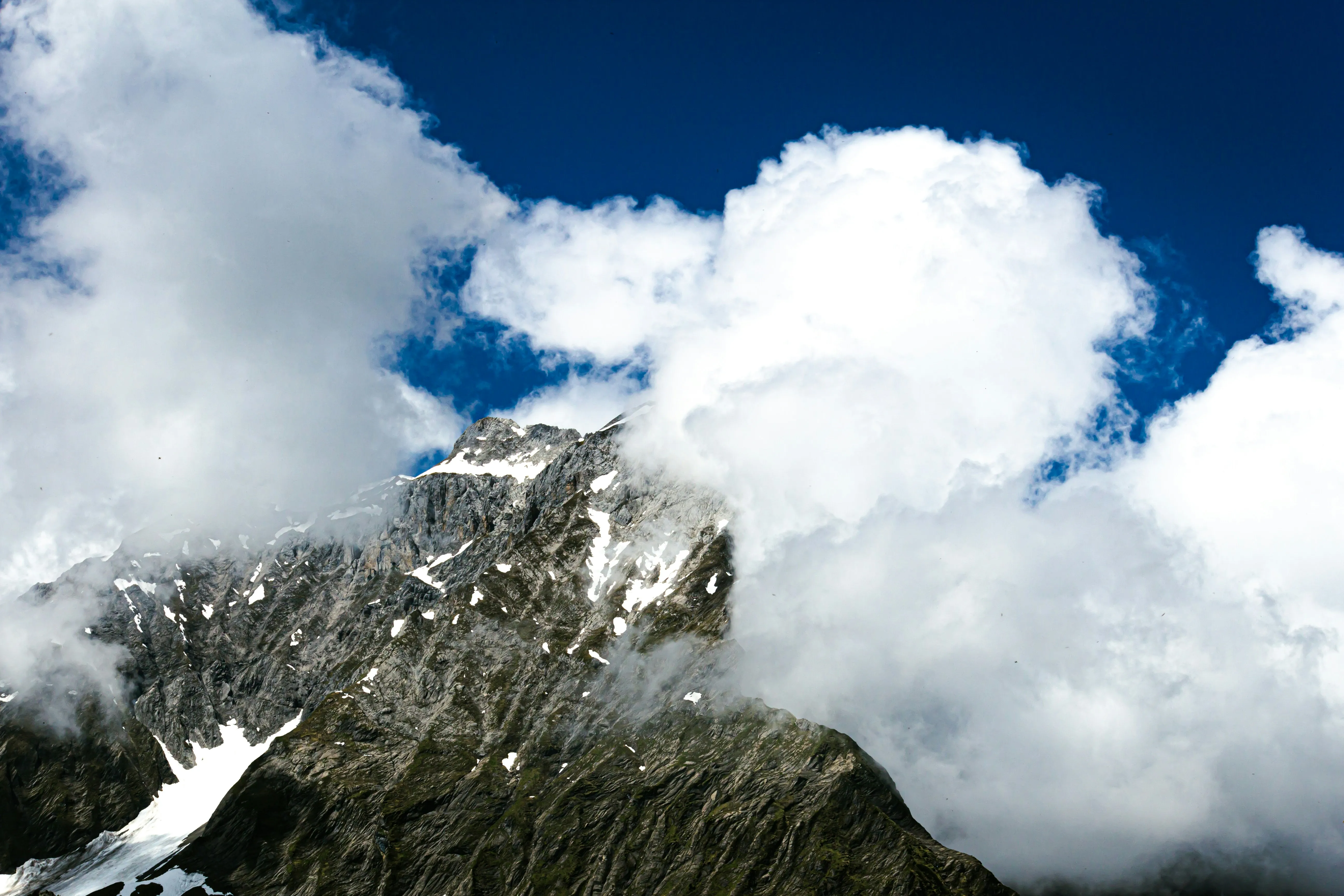 Mountain Peak Covered in Snow and Clouds Under Blue Sky