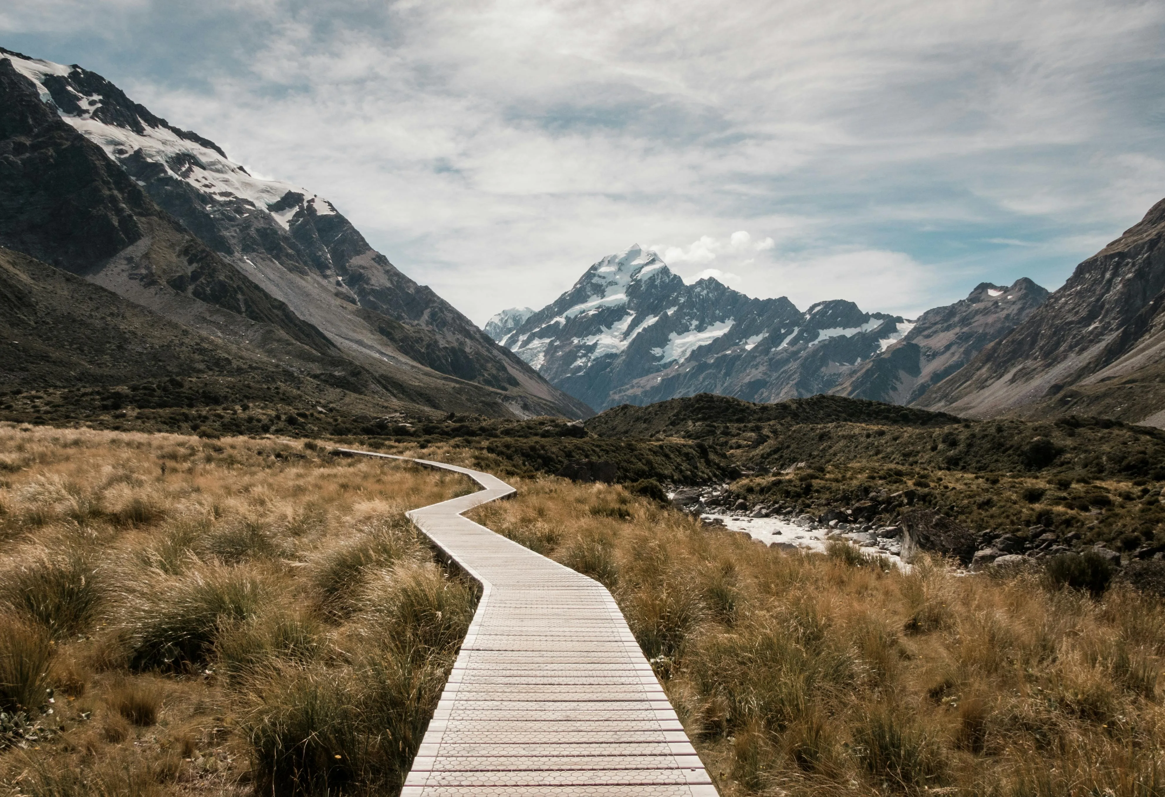 Mountain Road Leading To Snow Peaks Under Bright Blue Sky