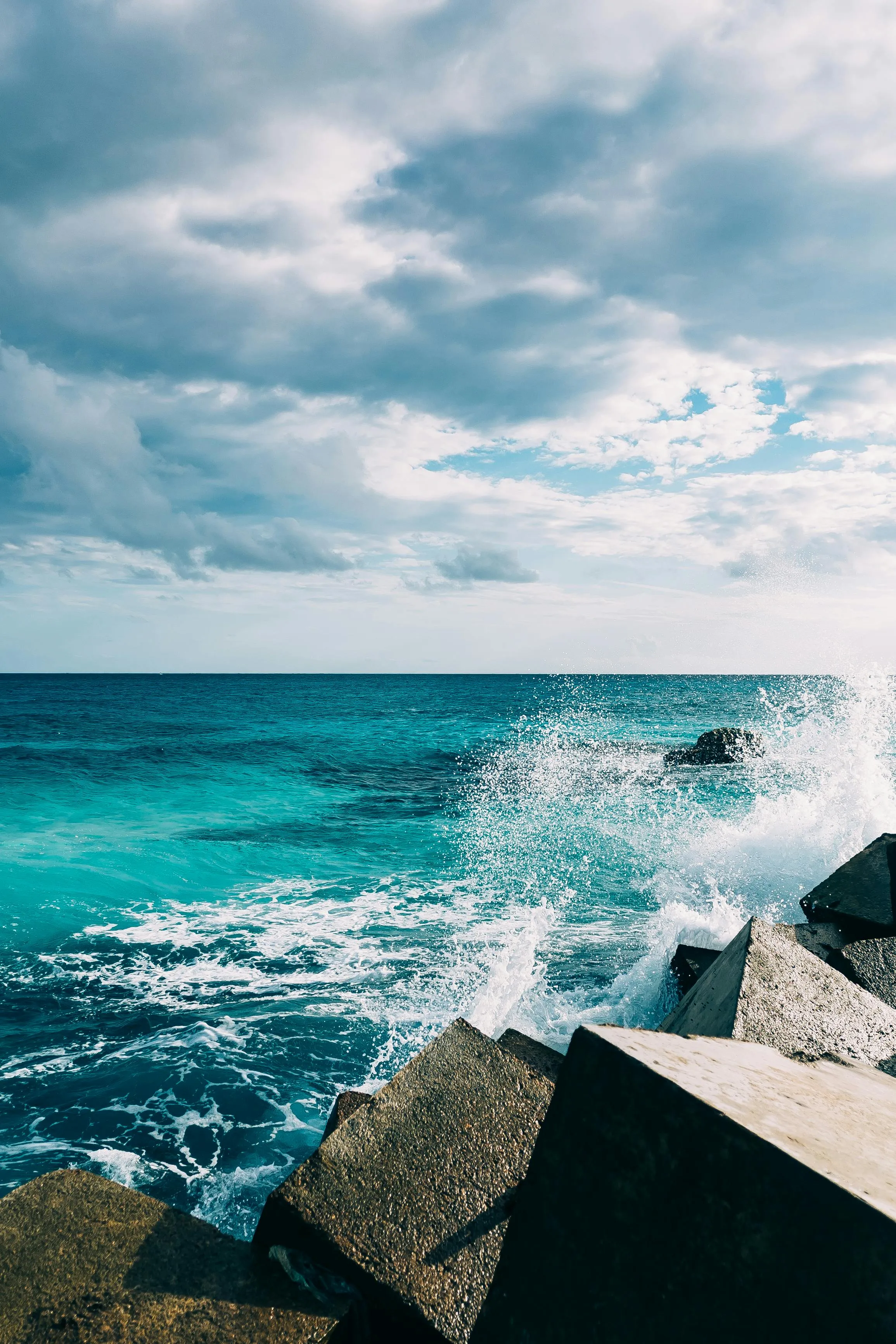 Ocean Waves Crashing Against Rocks Beneath Blue Sky