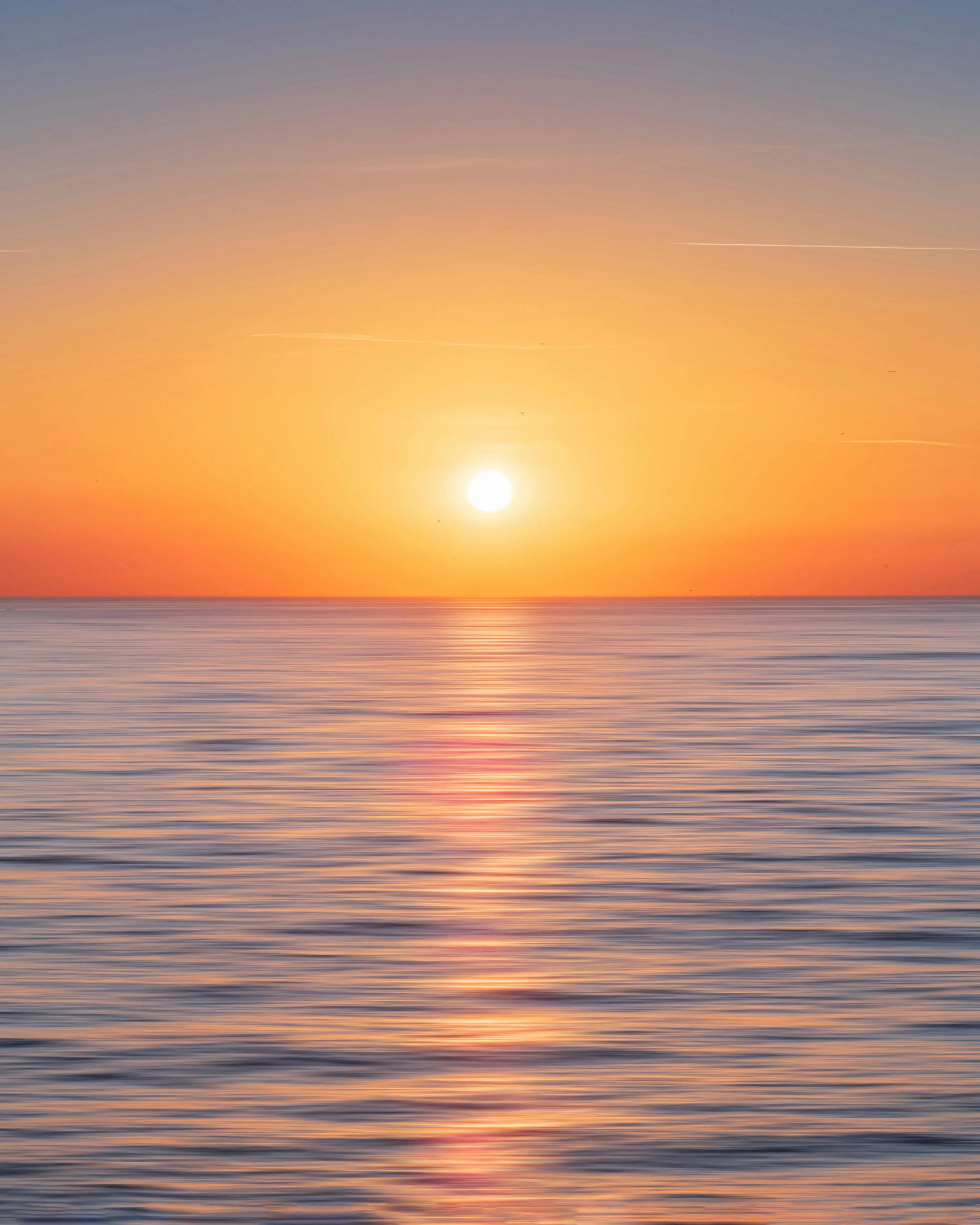 Orange Sun Setting Over Calm Ocean with Low Clouds Image