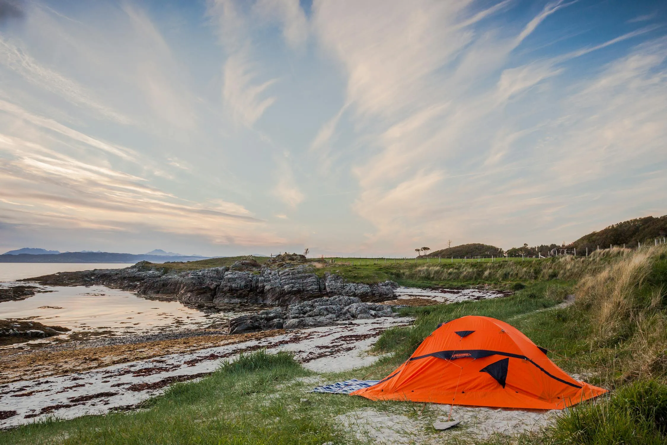 Orange Tent Set Up on Rocky Coastline Under Cloudy Sky