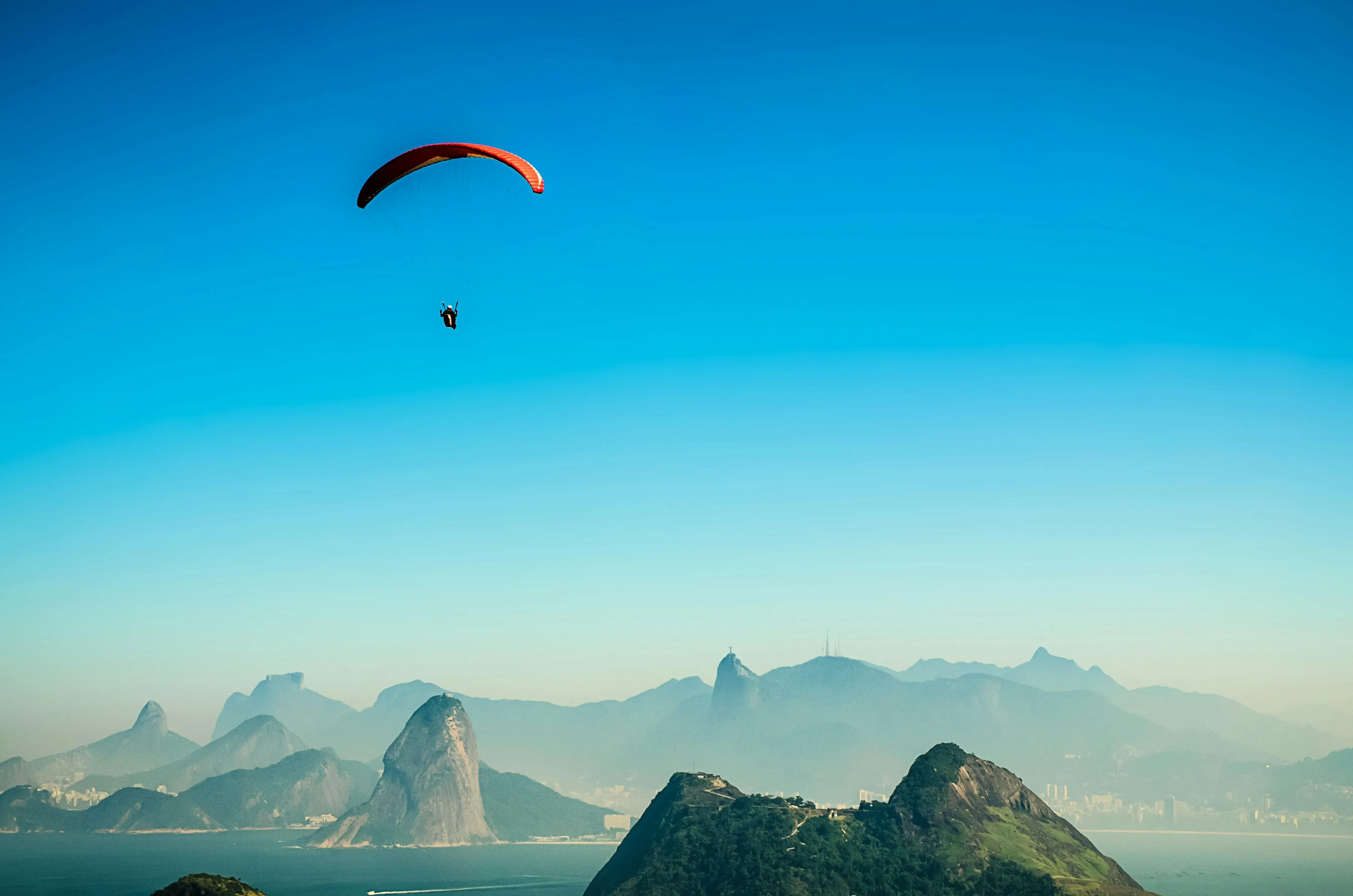 Paraglider Soaring Above Mountain Peaks and Clear Sky