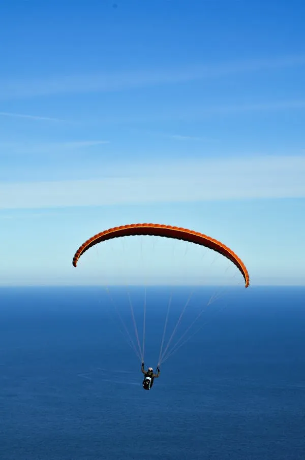 Paragliding Adventure Over Clear Blue Ocean Skies Wallpaper