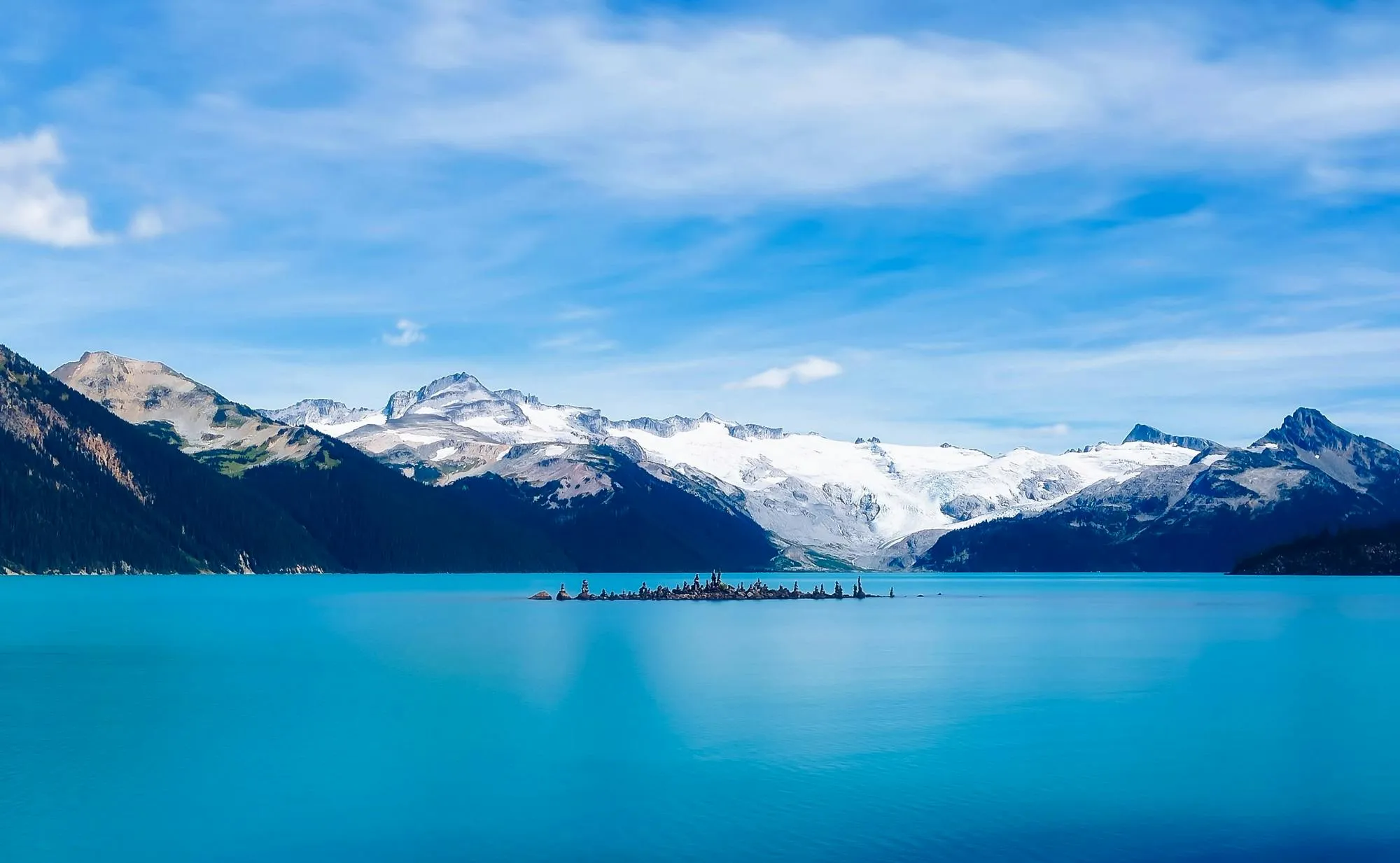 Peaceful Lake Surrounded By Snowy Mountains Under Blue Sky