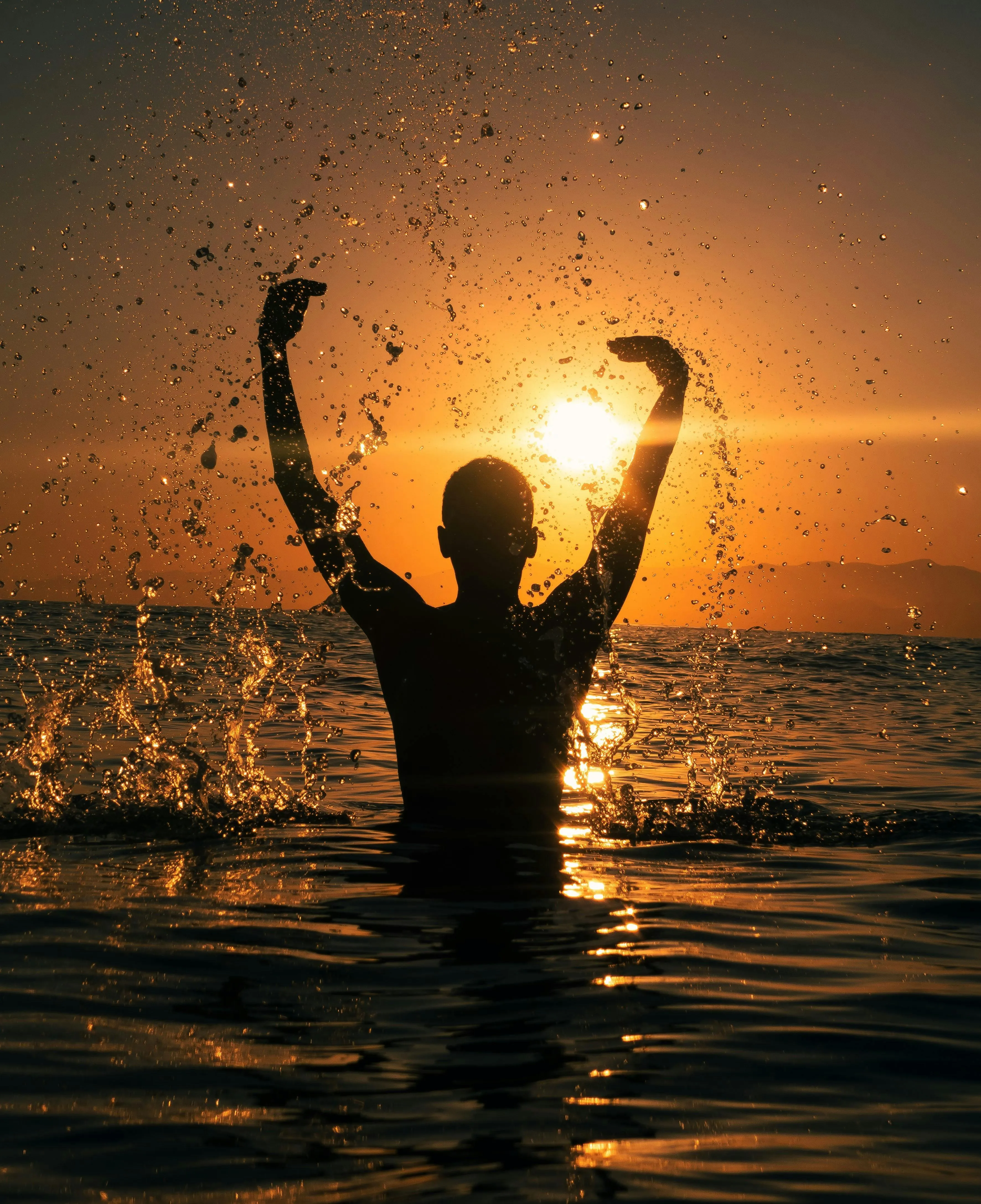 Person Celebrating Rain in Sunset with Raised Arms