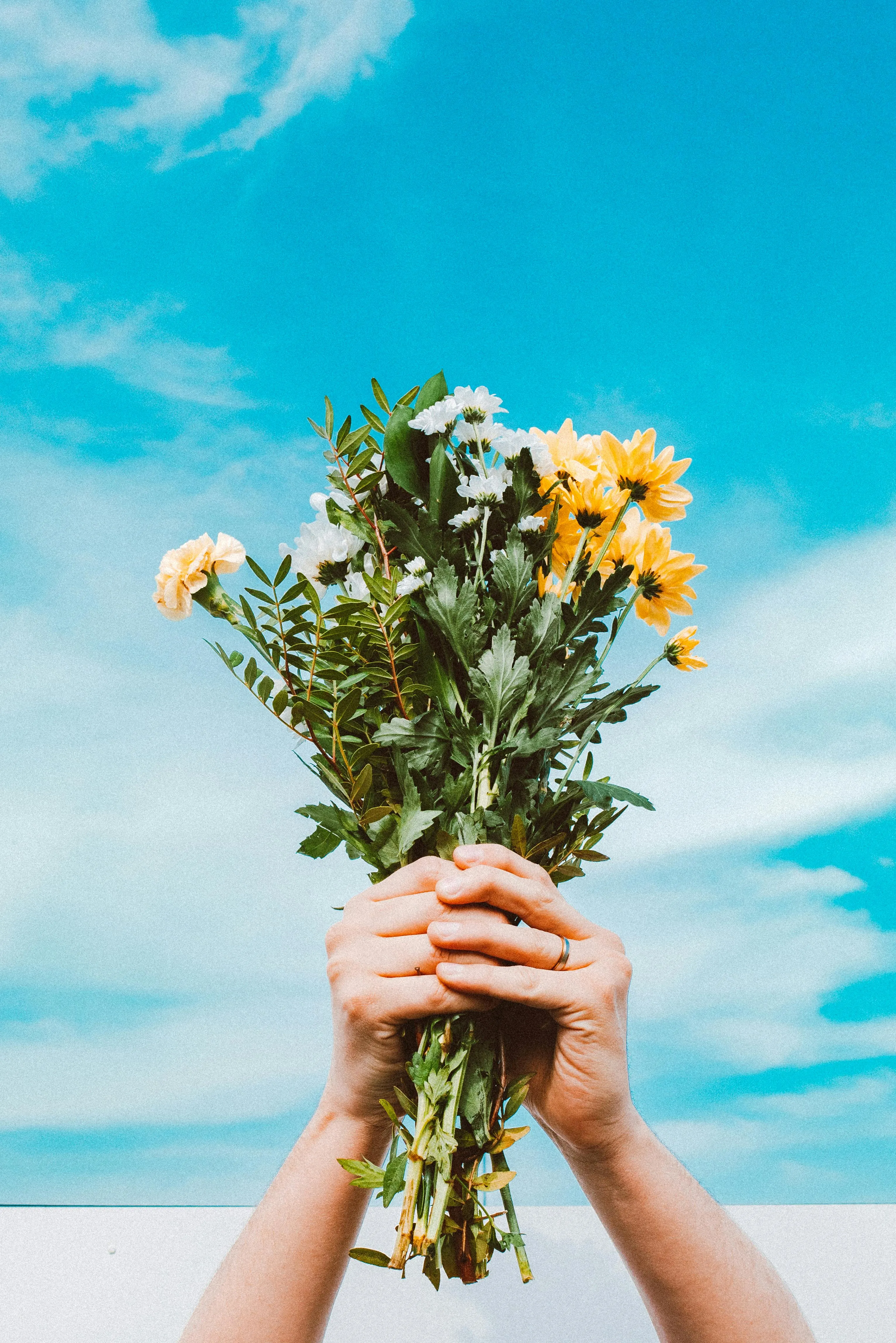 Person Holding Bright Flowers Under a Clear Blue Sky