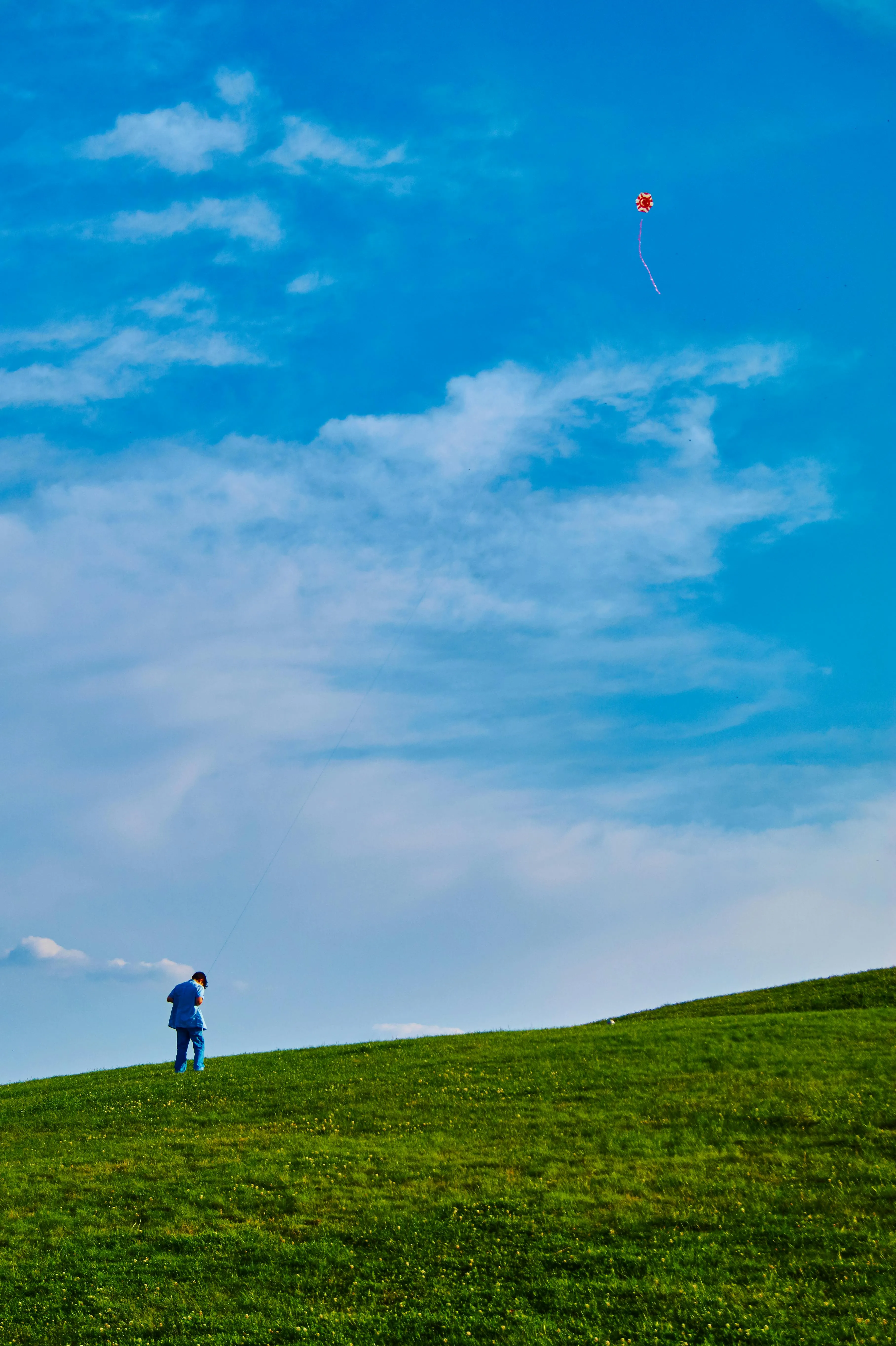Person Standing Alone on Green Hill Under Vibrant Blue Sky