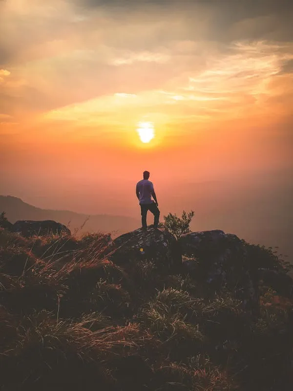 Person Standing on Hill Watching Sunset with Clouds
