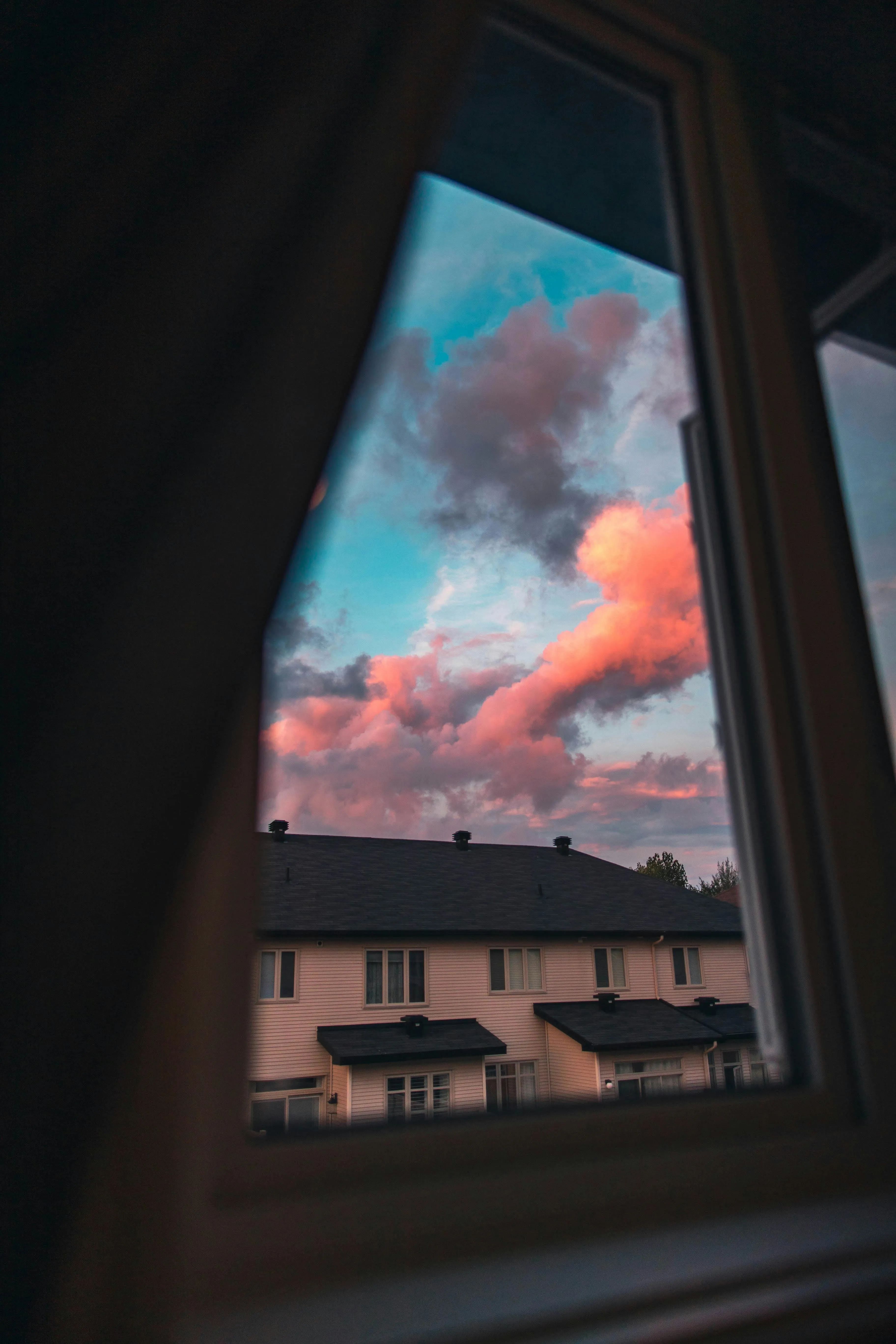 Pink Clouds Visible Through a Window Over Urban Rooftops