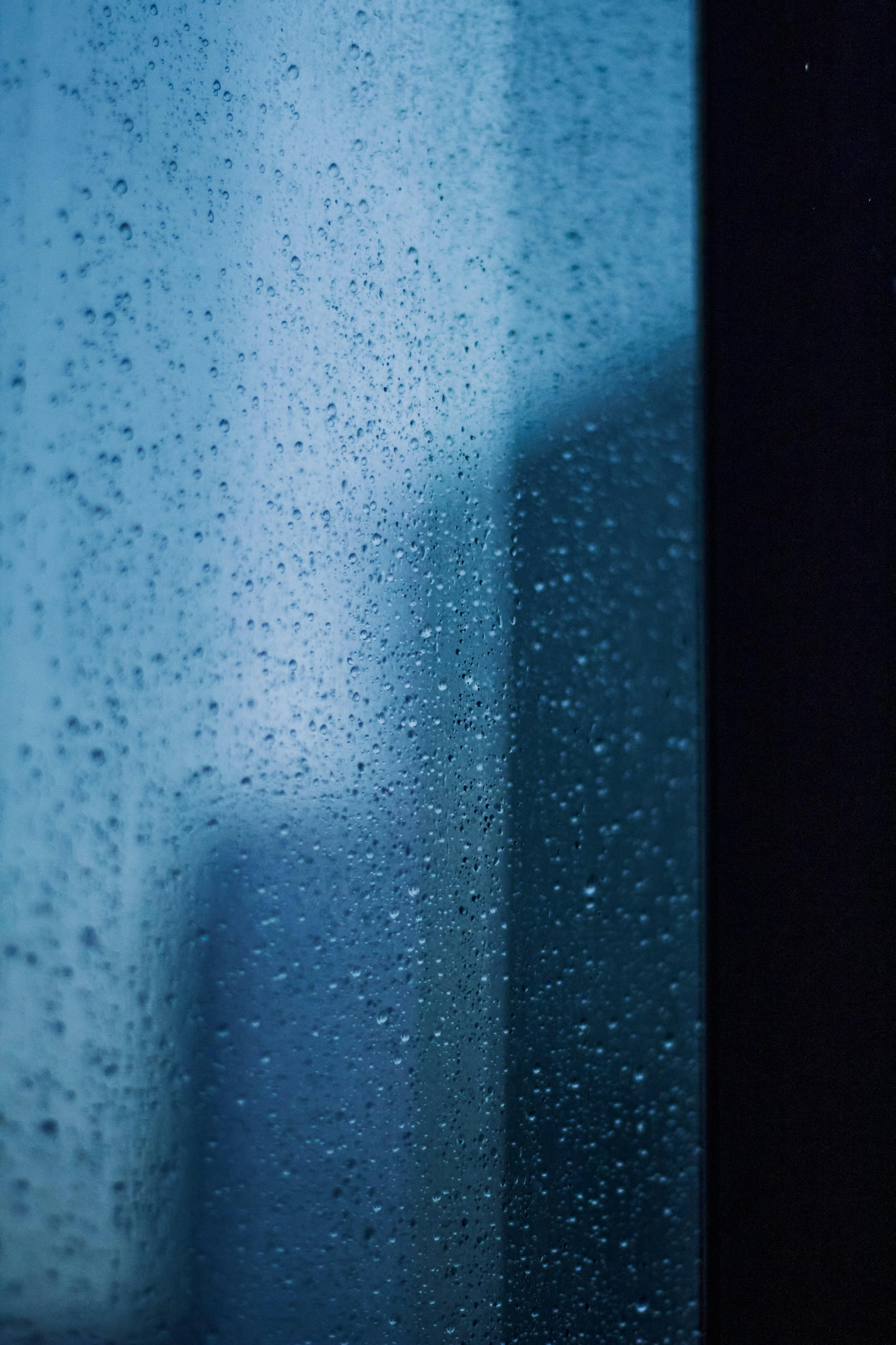 Rain Dripping Down Blue Glass Window in Close View