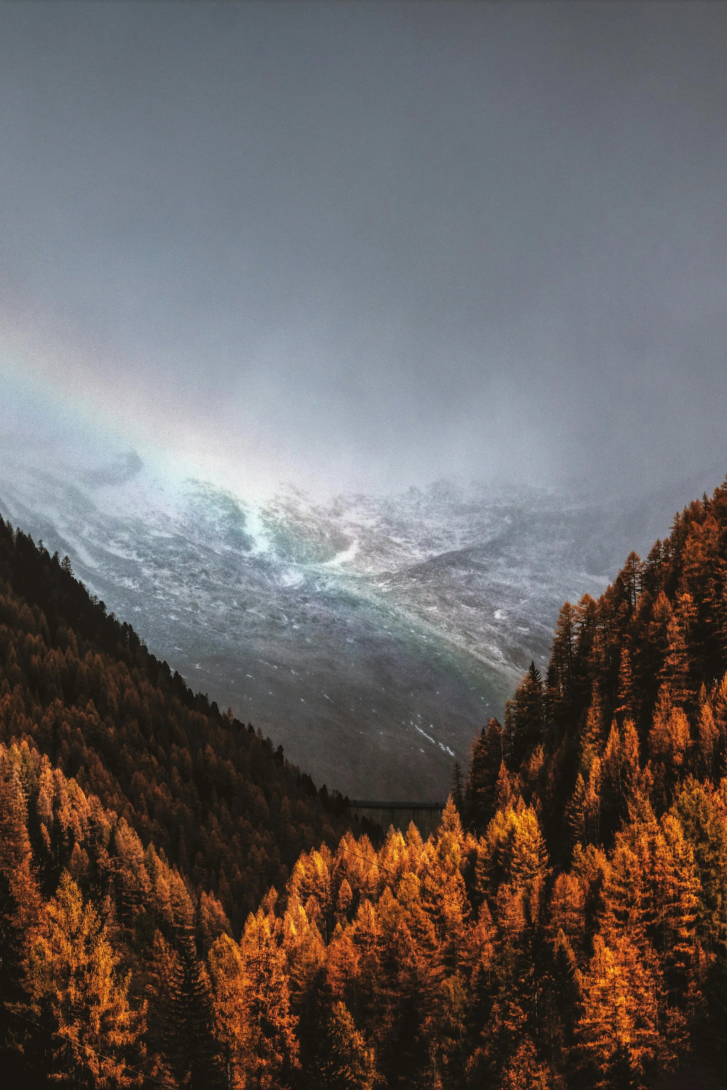 Rainbow Appears Over a Forested Valley Under Gray Skies
