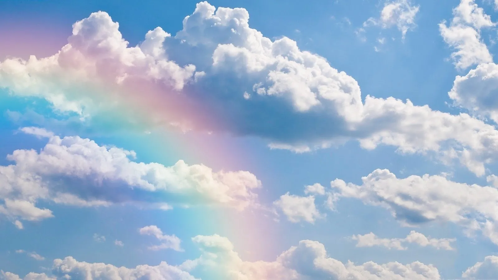 Rainbow Forming Between Soft White Clouds in Blue Sky