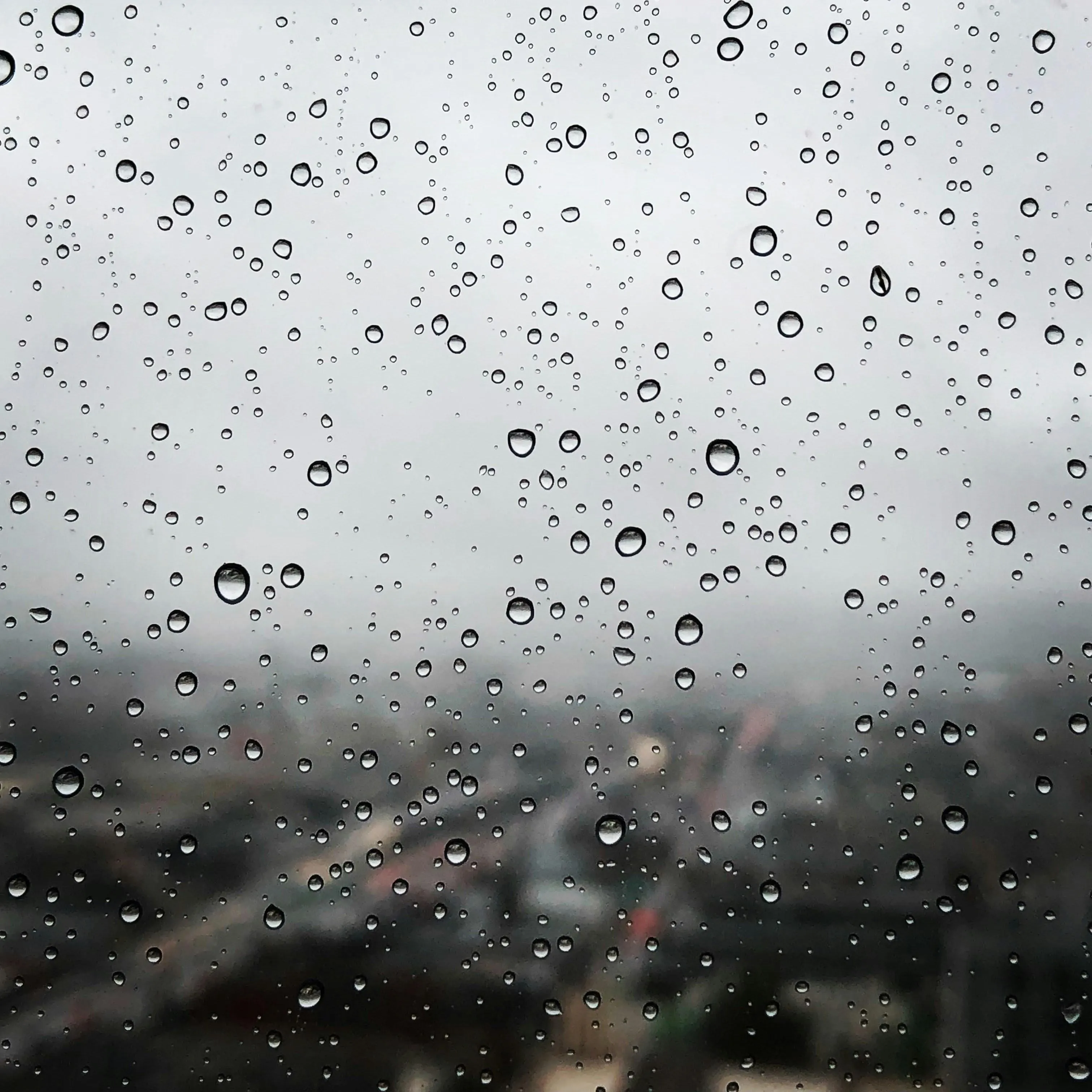 Raindrops on Window with Blurred Mountain and Cloudy Sky