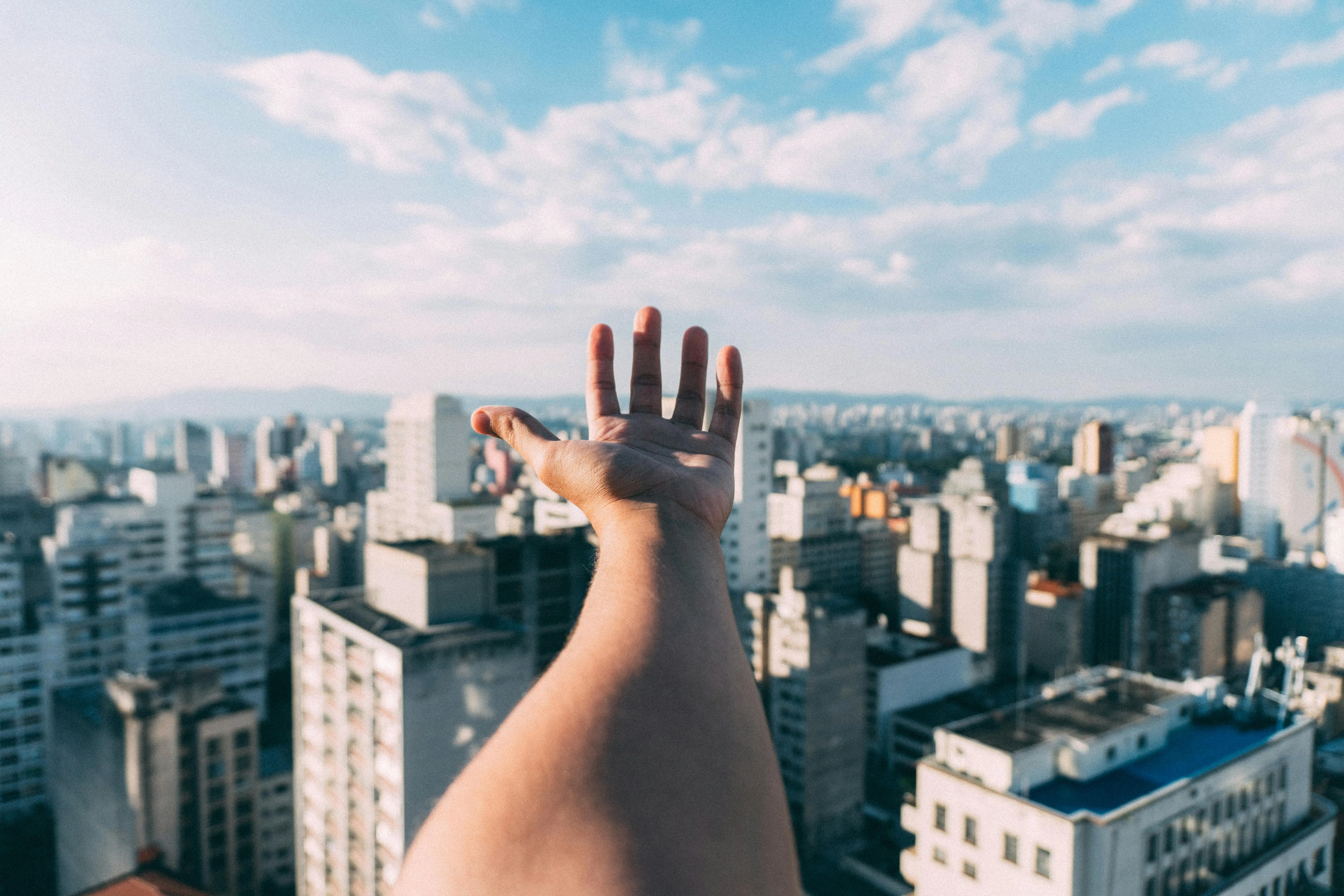 Raised Hands with City Skyline and Blue Cloudy Sky