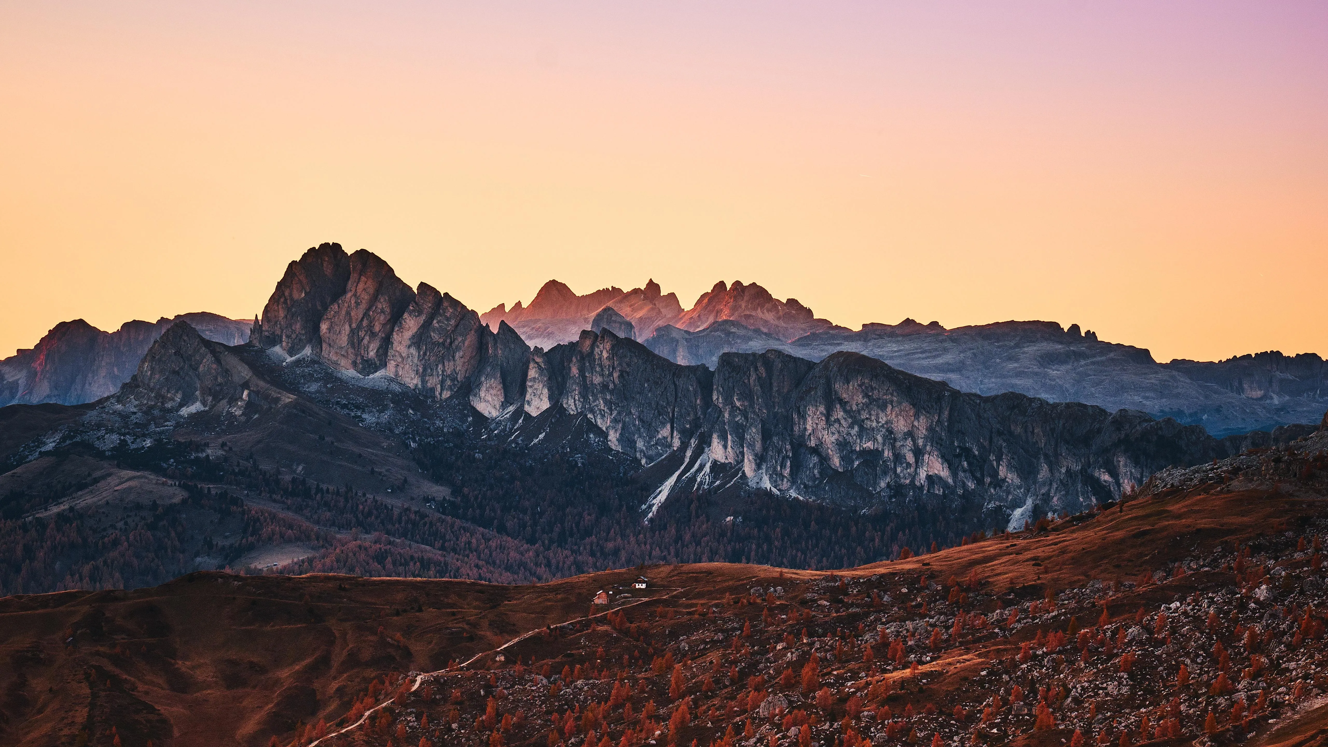 Rocky peaks with forest base under orange sky at dusk