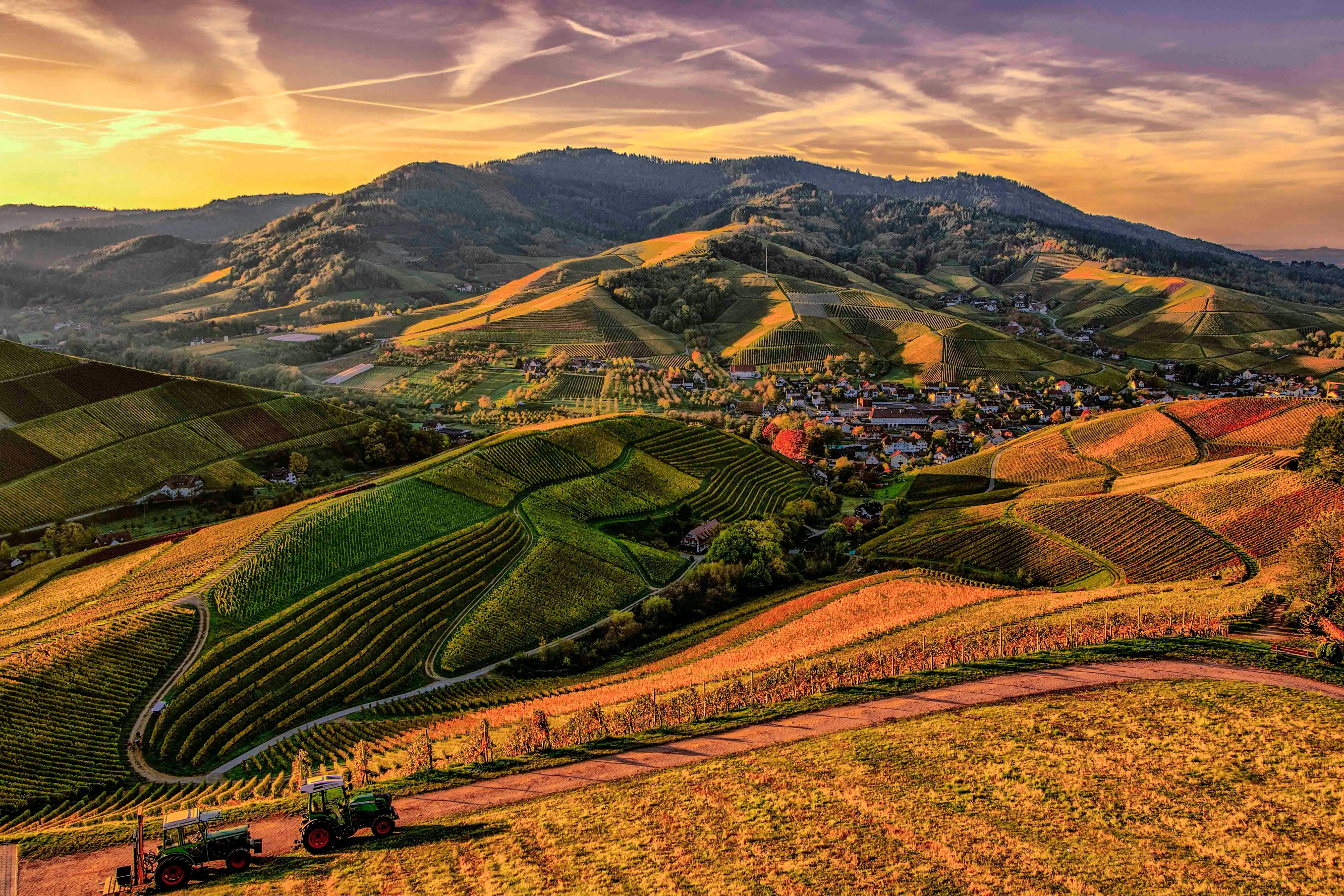 Rolling Hills with Green Fields Under Colorful Sunset Sky
