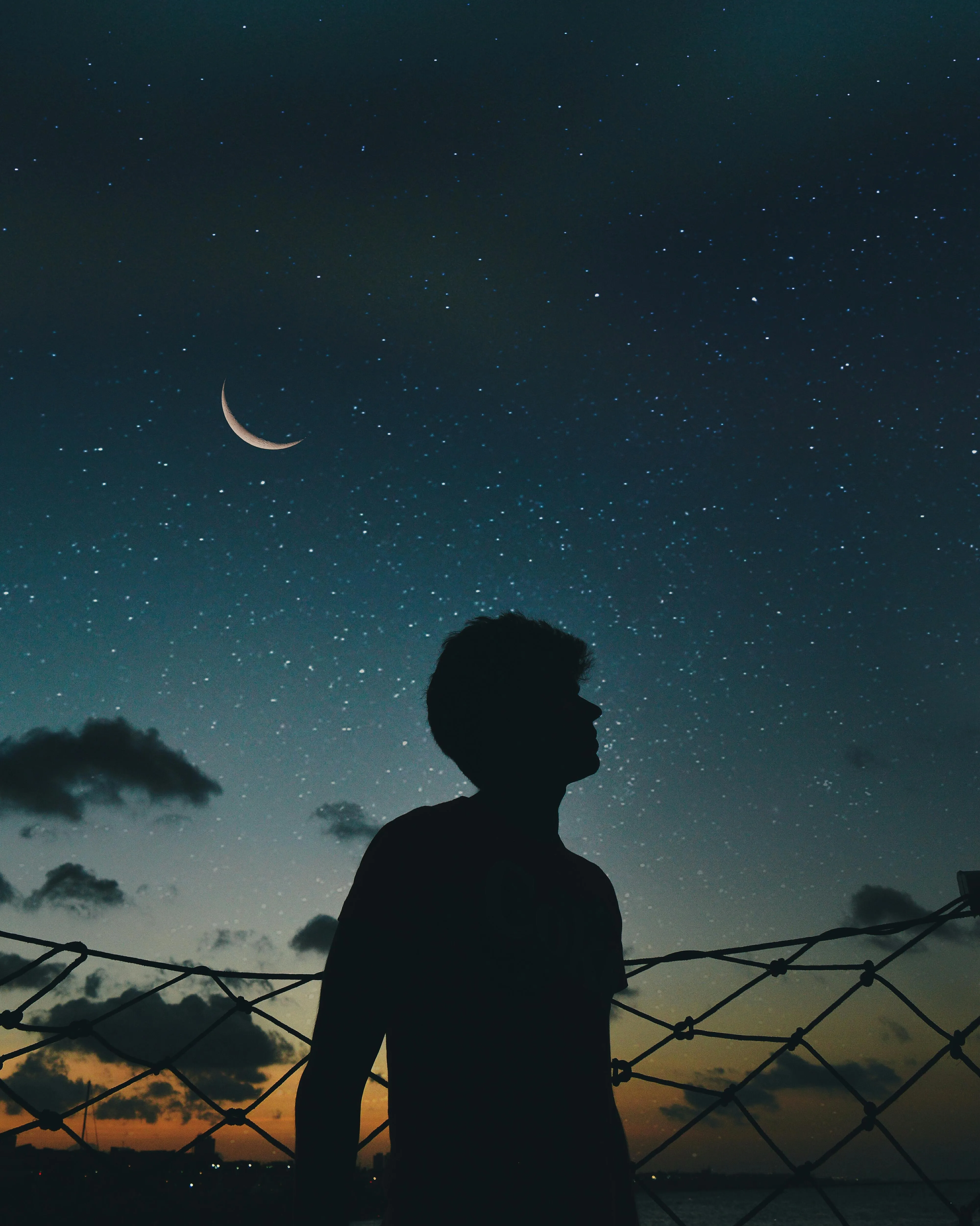 Silhouetted Man Under Crescent Moon and Evening Sky