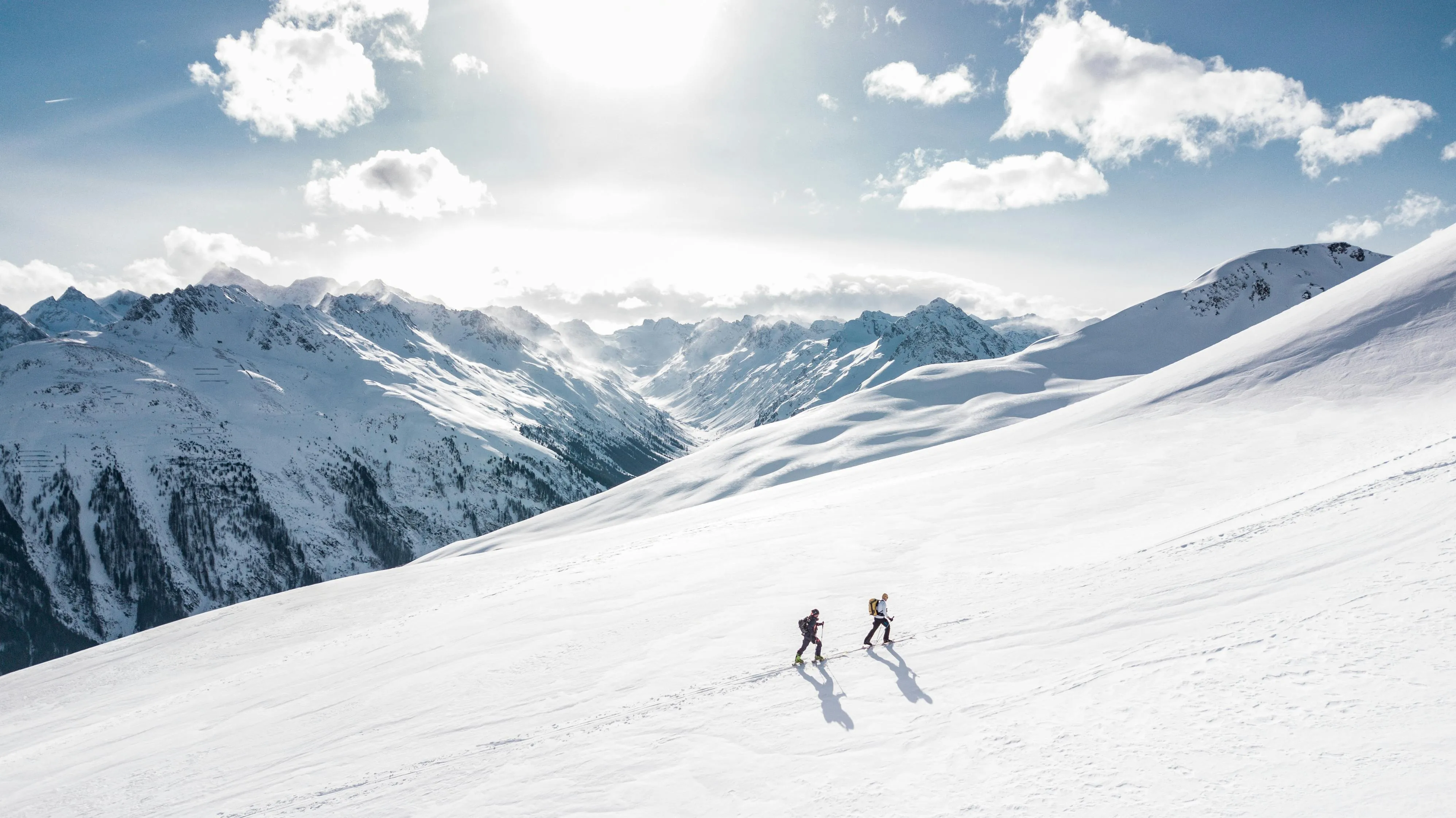 Skiers Moving Down a Snowy Mountain Under Cloudy Blue Skies