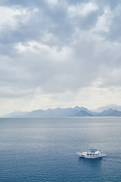 Small Boat Floating on Calm Sea Under Cloudy Sky Wallpaper