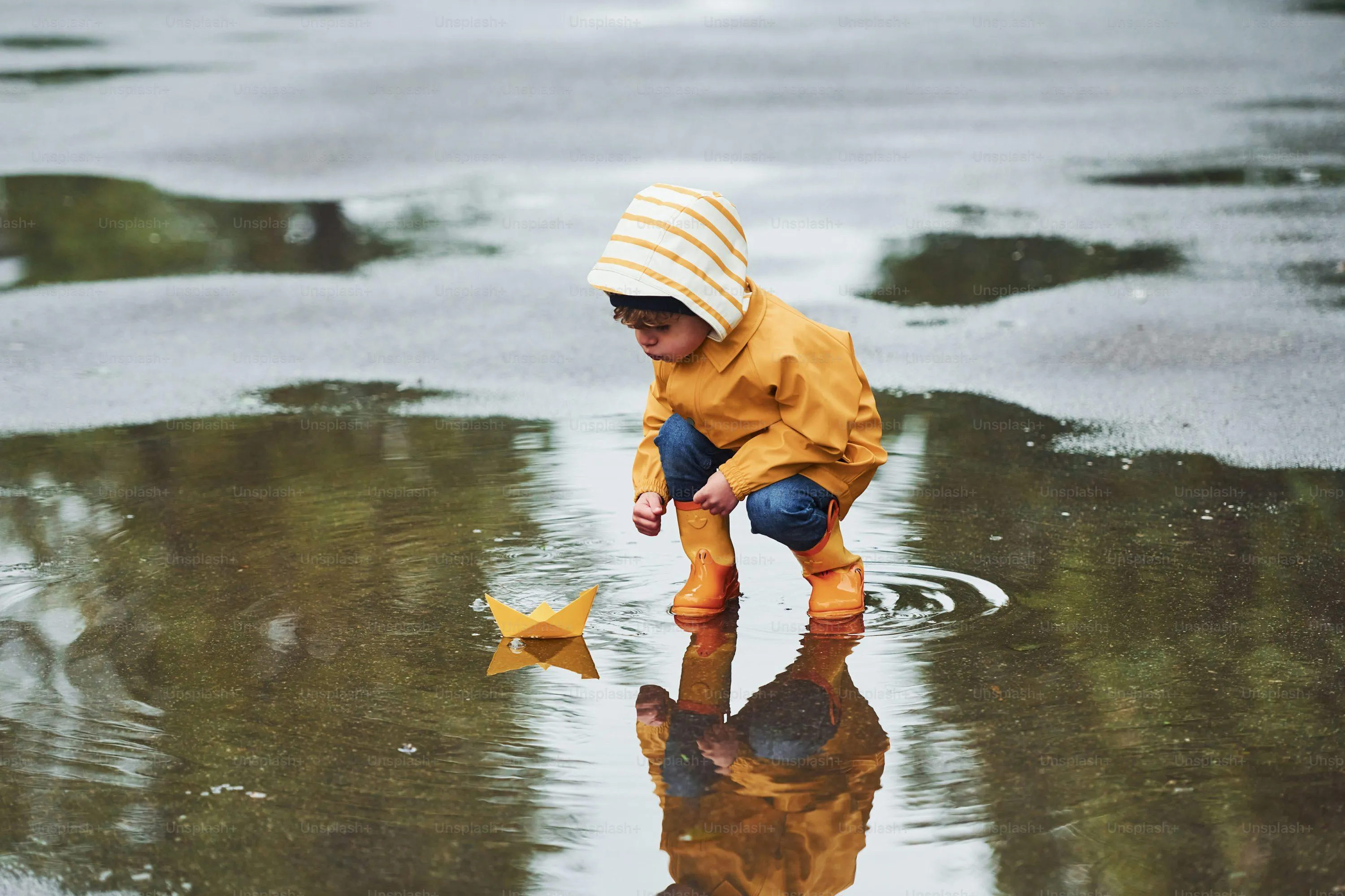 Small Child Wearing Yellow Raincoat Playing in Puddles
