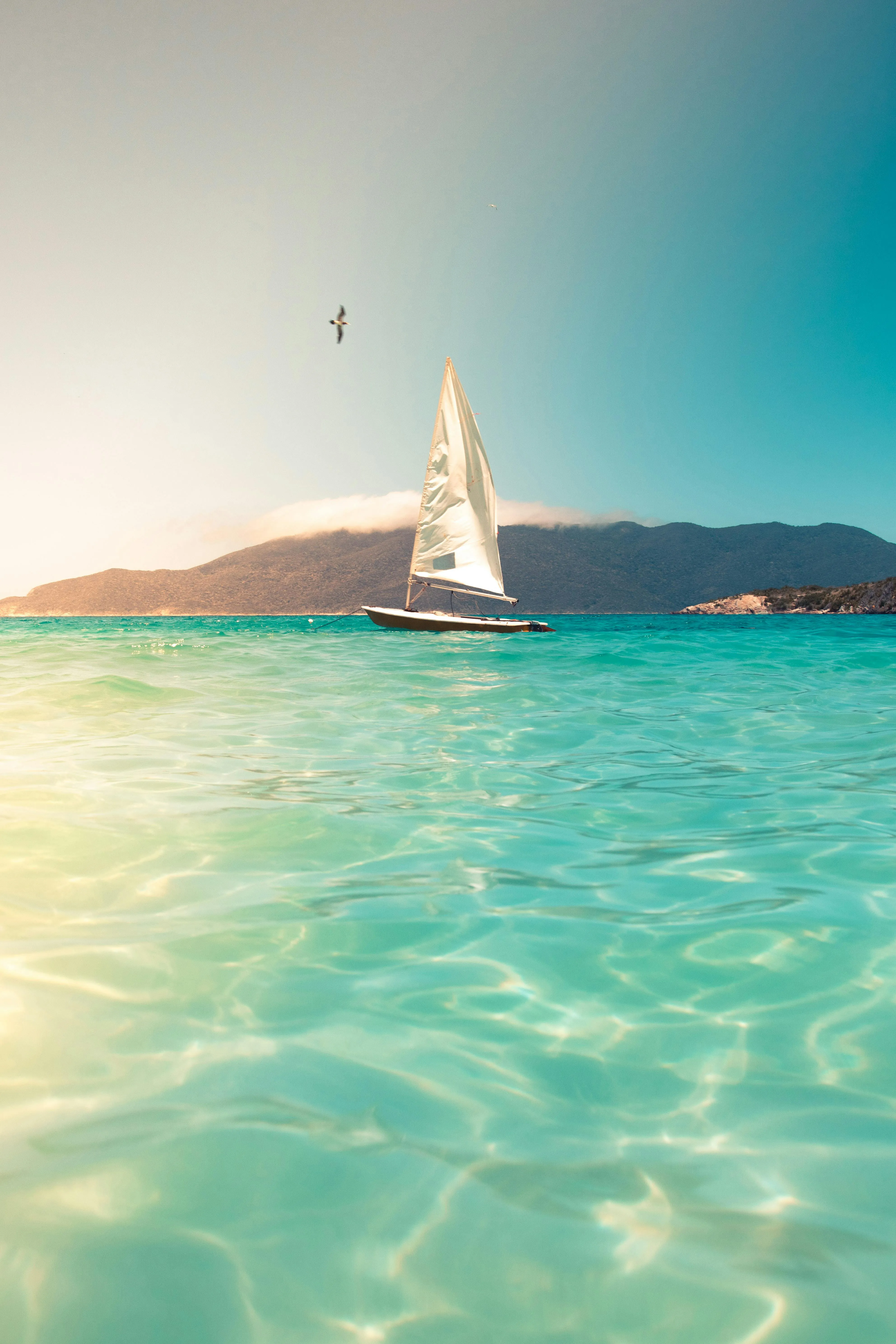 Small Sailboat Floating on Turquoise Water Under Sun