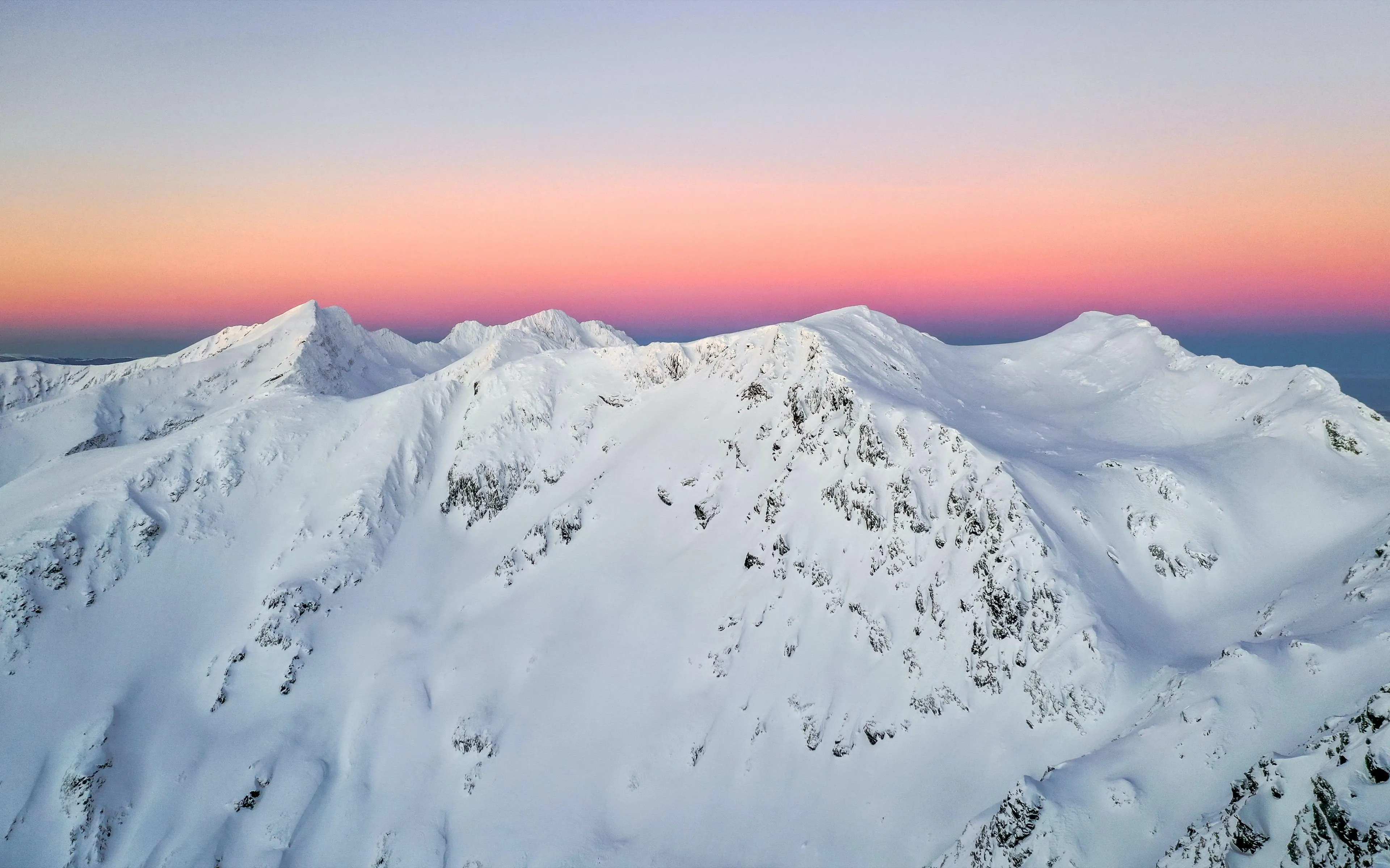 Snowcovered mountain peaks under soft pink and blue sky