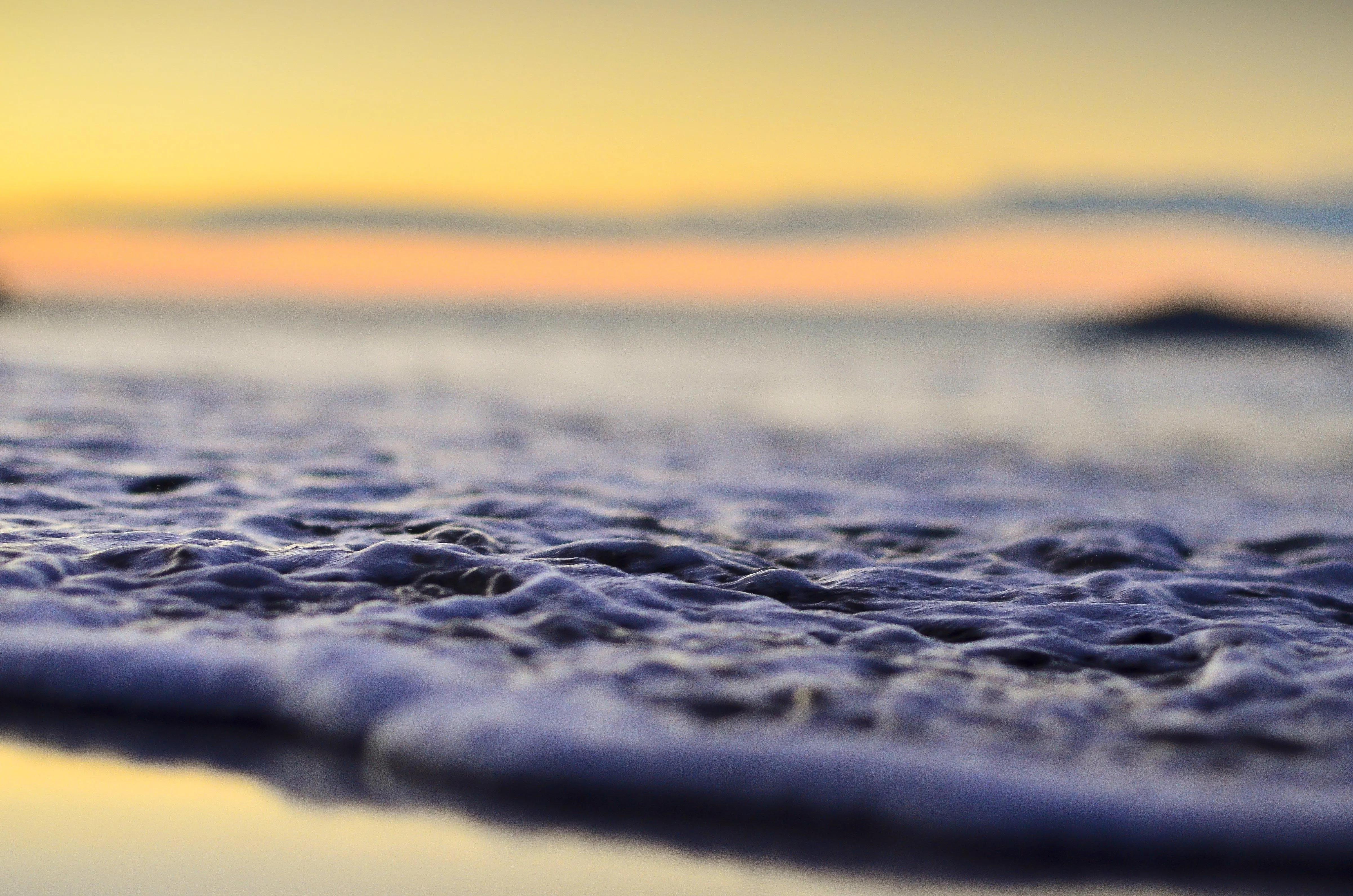 Soft waves rolling on beach under golden sunset Wallpaper