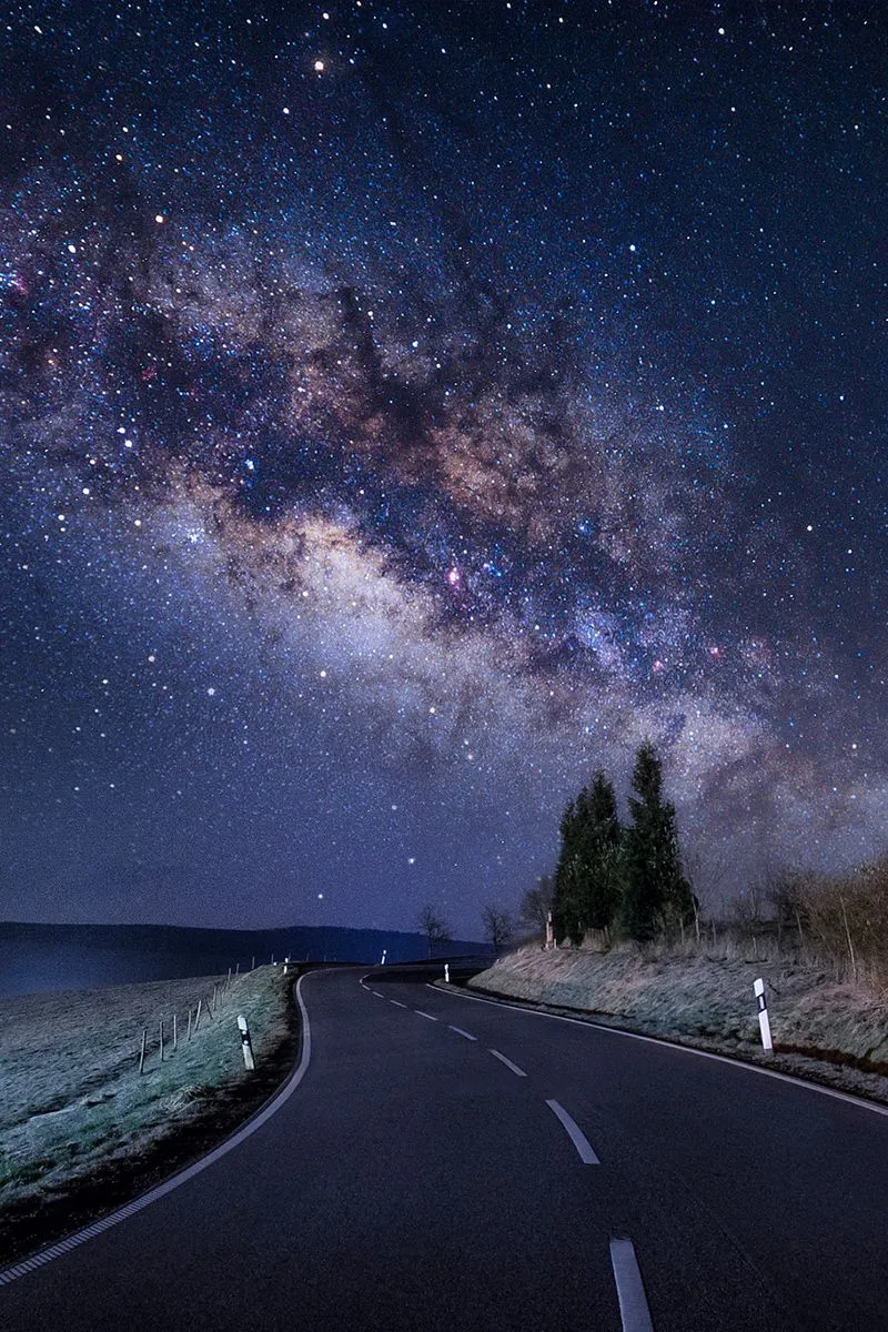 Starry Night Sky Over Empty Road Leading Into Distance