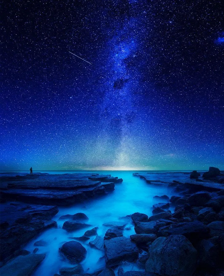 Starry Night Sky Over Rocky Beach with Blue Light