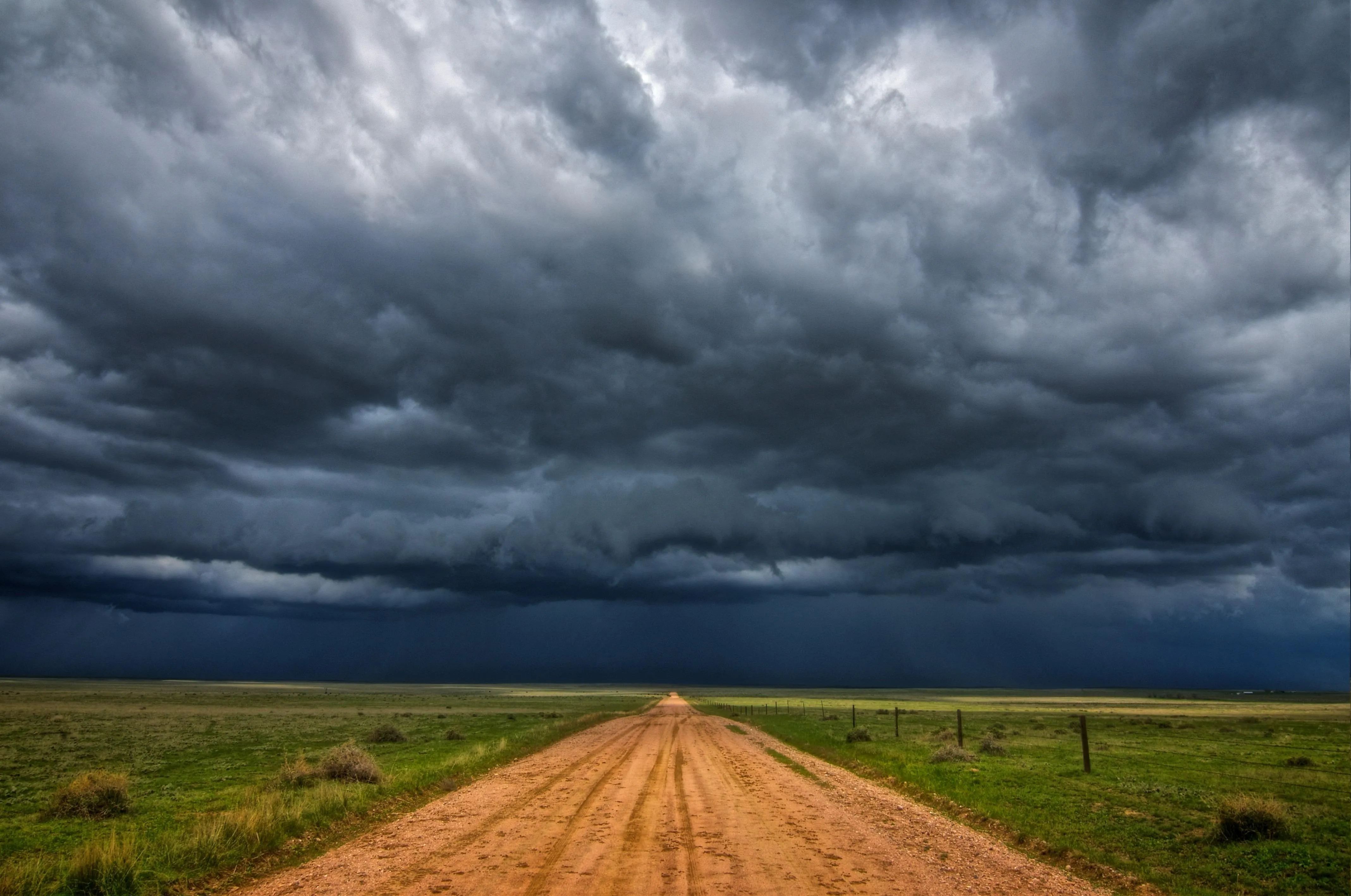 Storm Clouds Gathering Over Dirt Road in Green Field