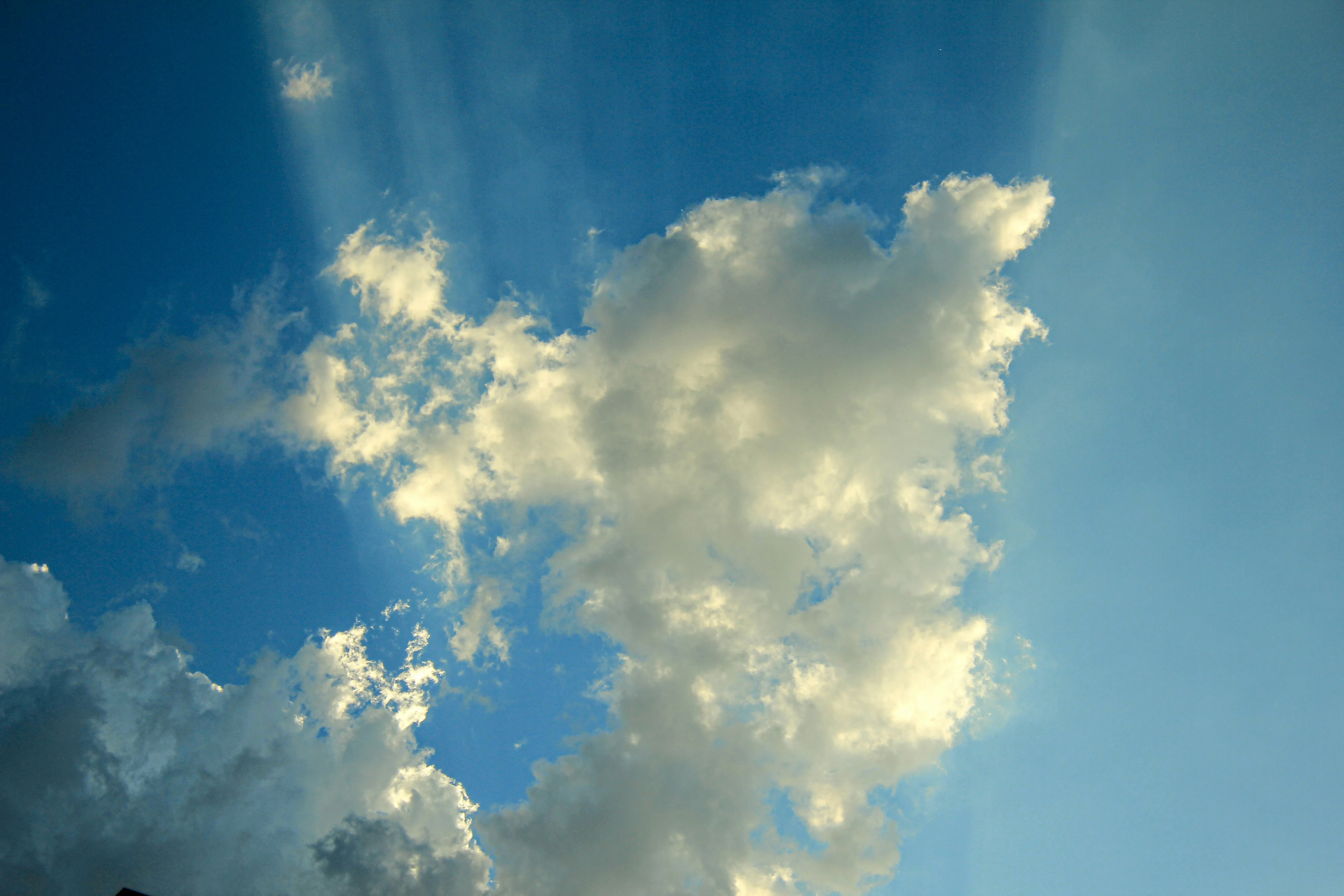 Sun Rays Piercing Through Clouds in Bright Blue Sky