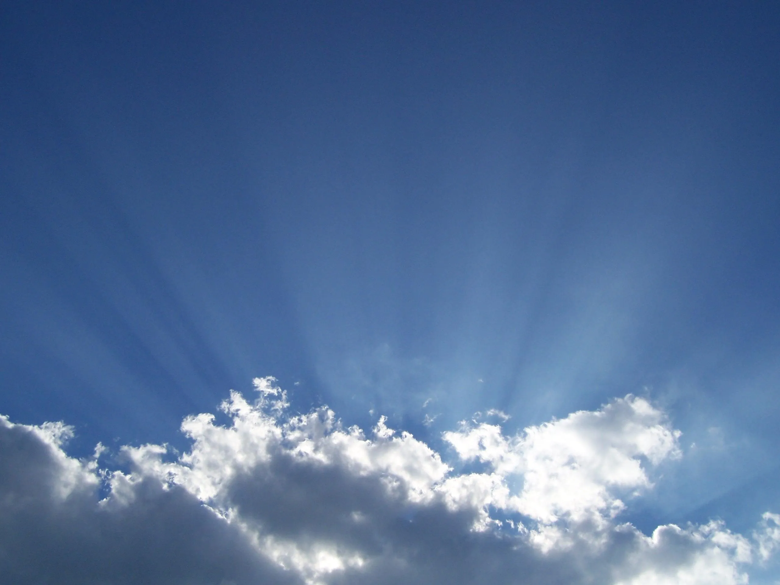Sun Rays Piercing Through Soft White Clouds in a Blue Sky