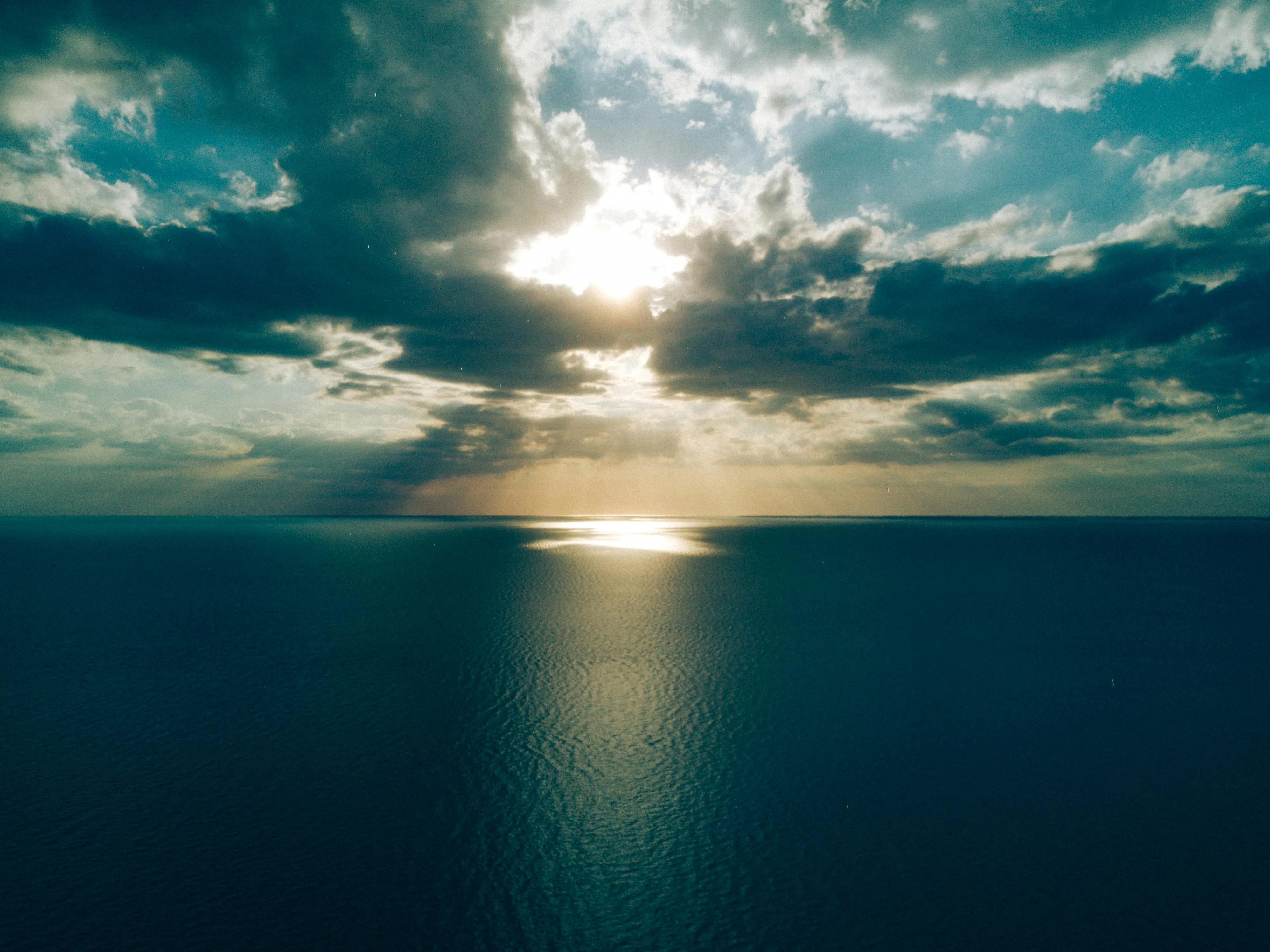 Sunset Over Calm Ocean with Rays Breaking Through Clouds