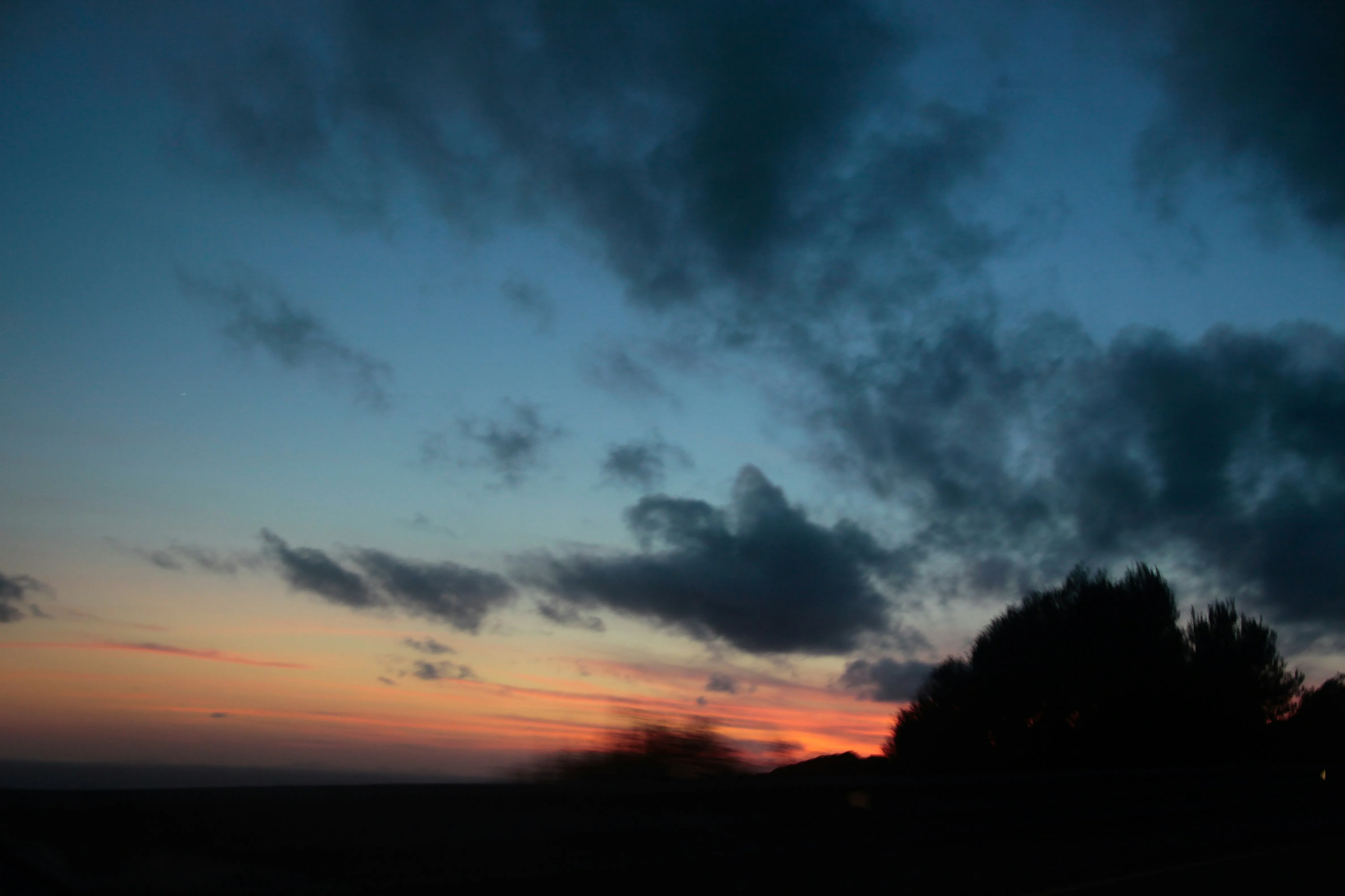 Sunset with Dark Clouds Over Silhouetted Trees in Distance