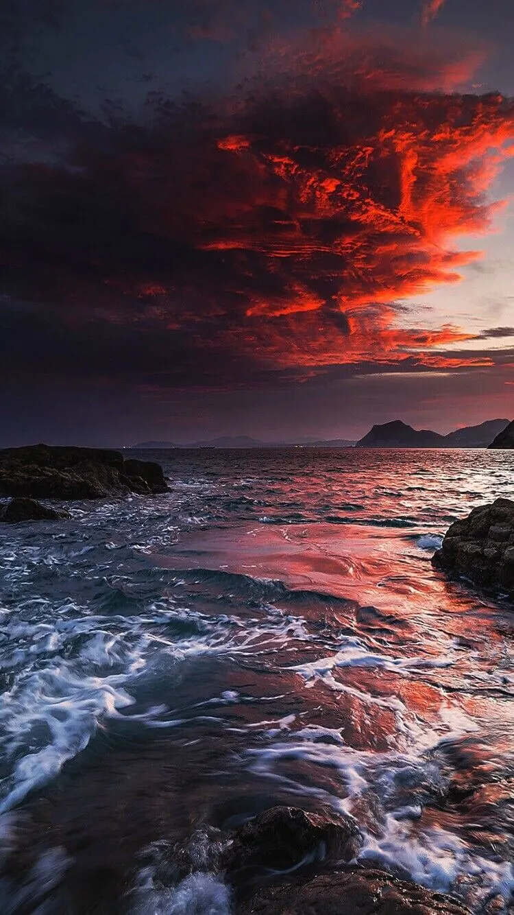 Vivid Sunset Sky with Dark Clouds Over Rocky Beach Image