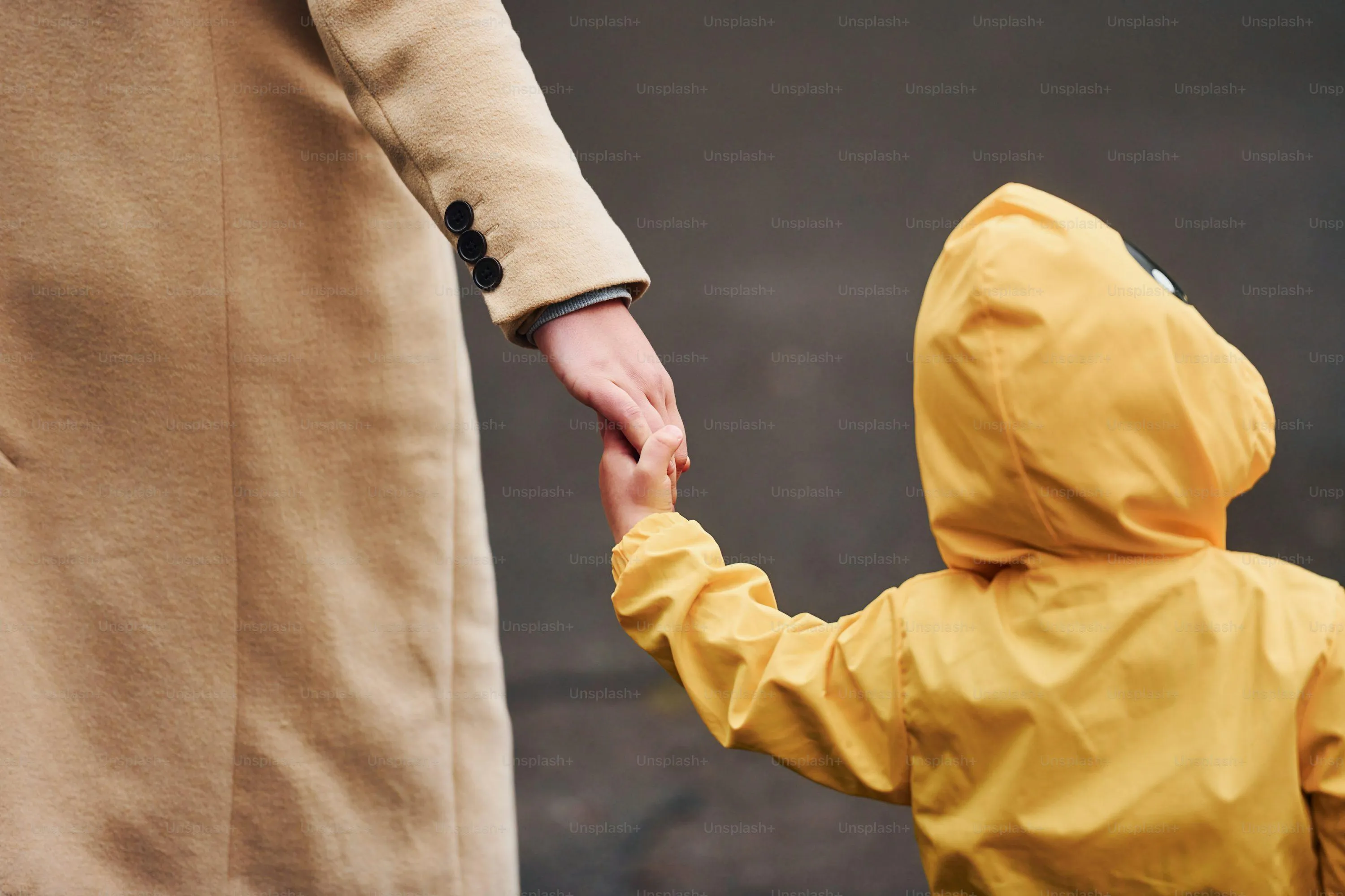 Woman Holding Childs Hand in Yellow Coat Under Rain