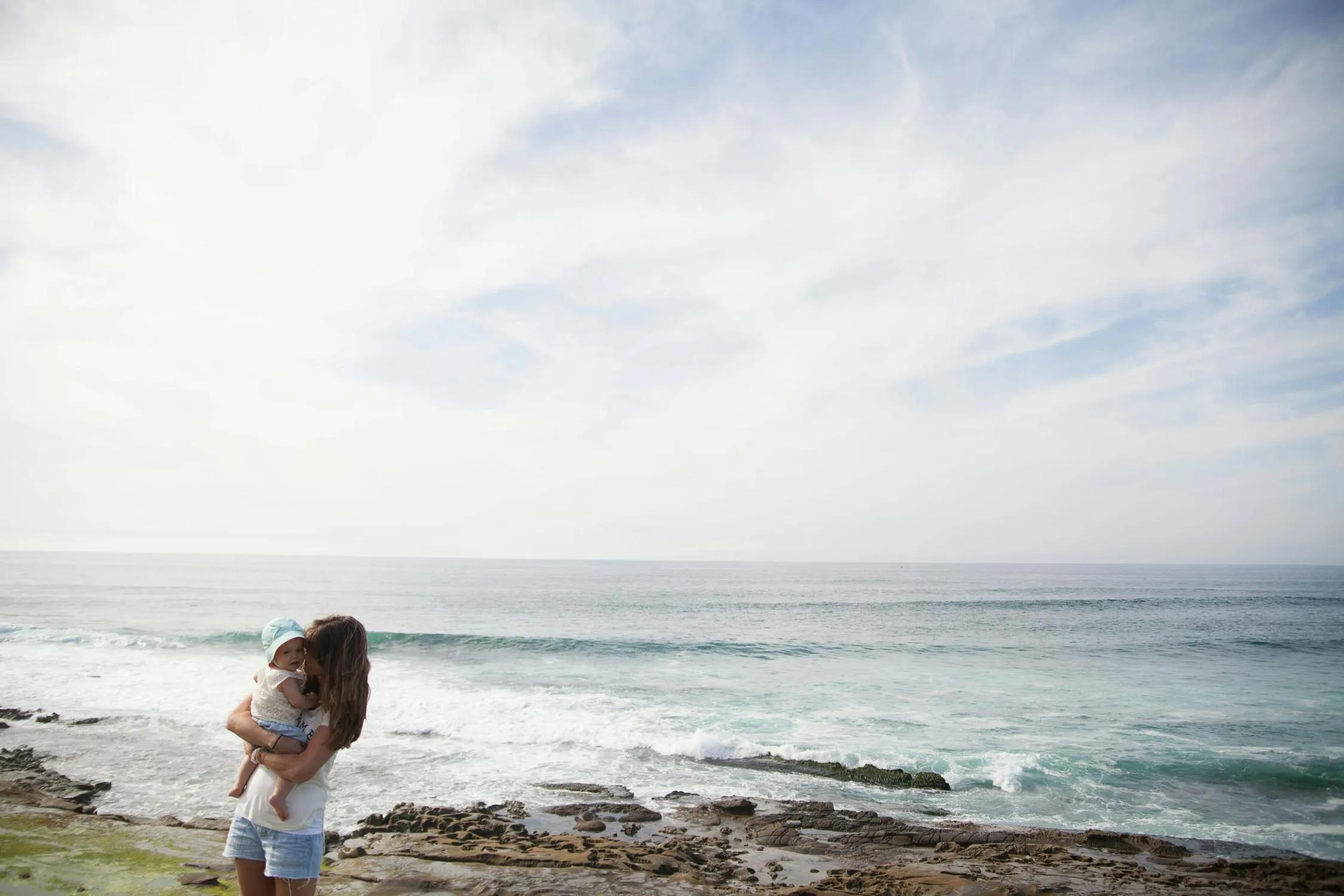 Woman Standing with Baby Near Ocean on a Cloudy Bright Day