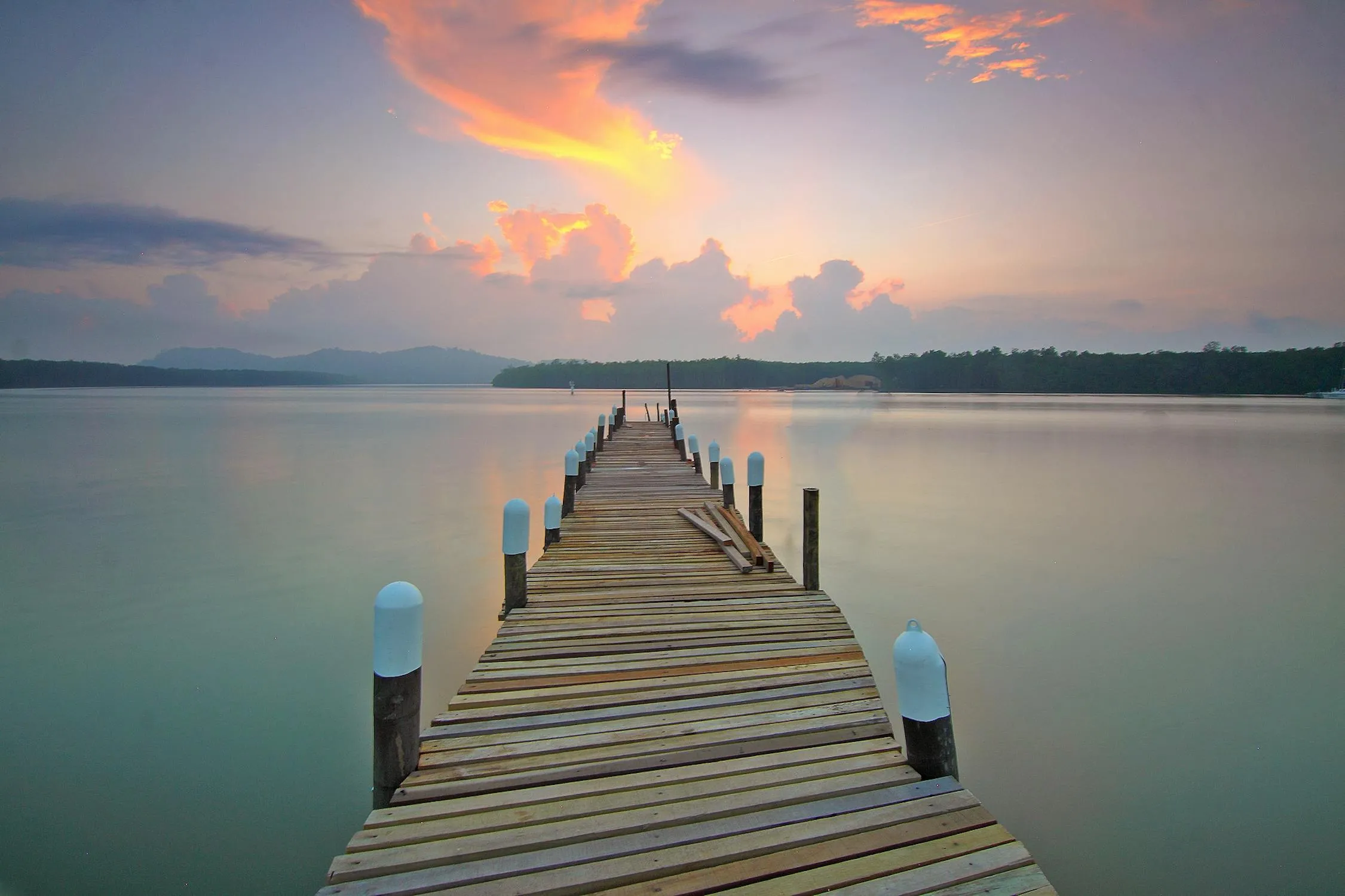 Wooden Pier Leading Into Calm Water Under Colorful Sunset